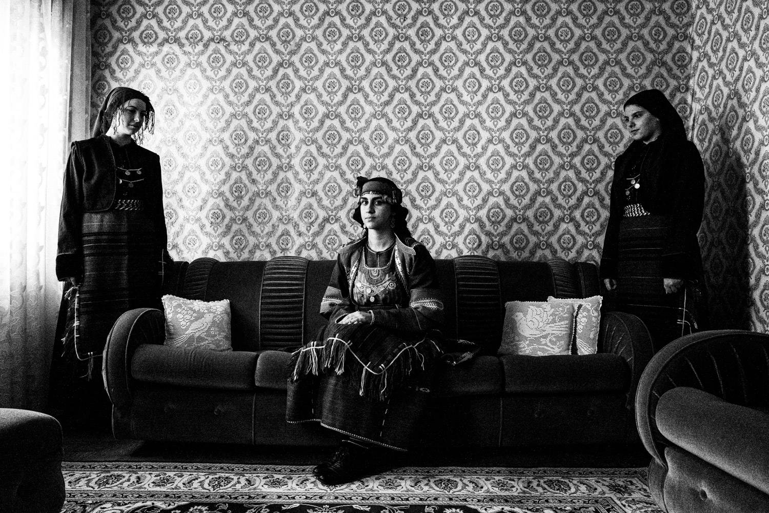 Three women inside the living room of a traditional house, wearing the traditional dresses. Drymos, Thessaloniki, Macedonia, Greece. Black and white photograph by George Tatakis