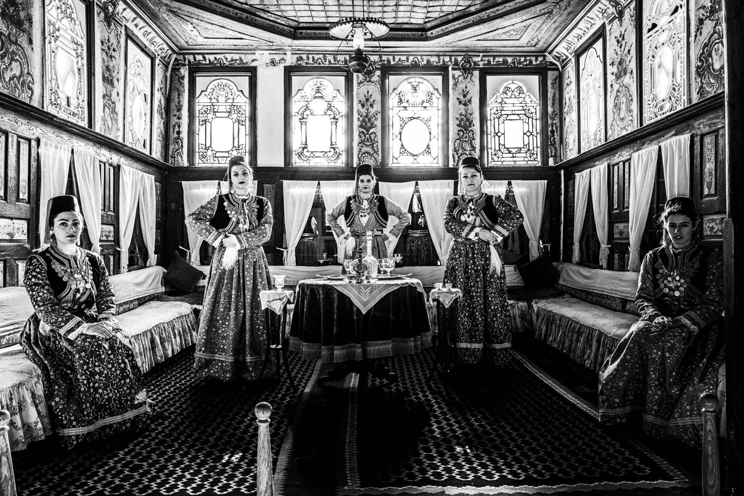 A group of women posing inside a local traditional mansion. Kastoria, Macedonia, Greece. Black and white photograph by George Tatakis