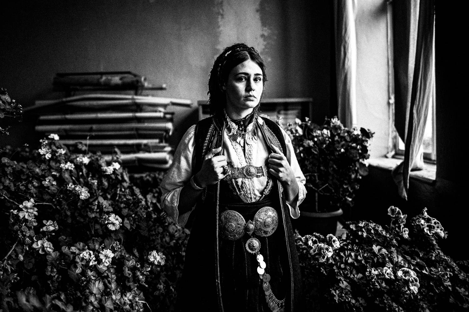 Portrait of a woman amidst Geranium flowers, wearing the local folklore dress. Polypotamos, Florina, Macedonia, Greece. Black and white photograph by George Tatakis