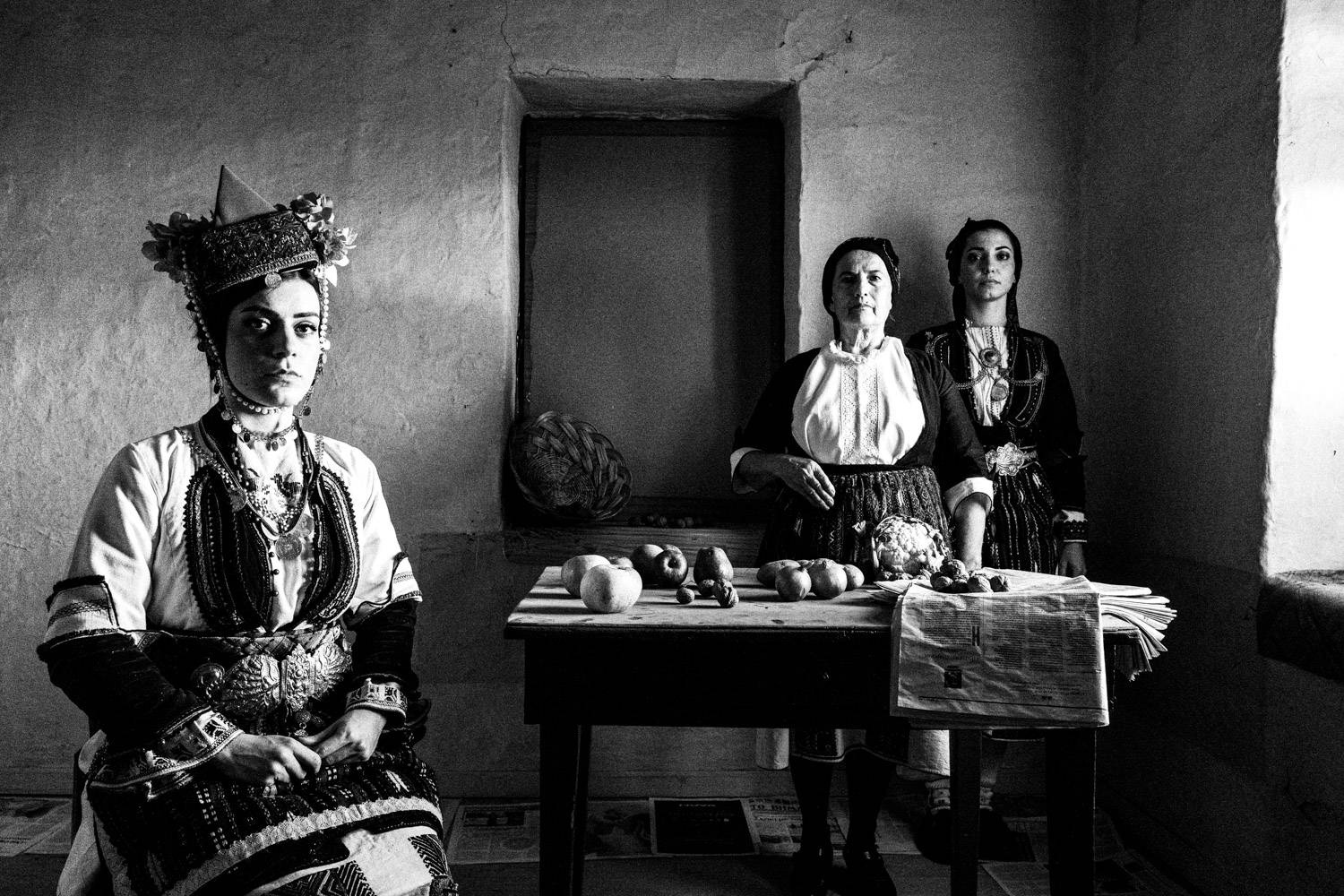 Portrait of three women inside a local abandoned house, wearing the folklore dresses. Aggelochori, Naoussa, Macedonia, Greece. Black and white photograph by George Tatakis