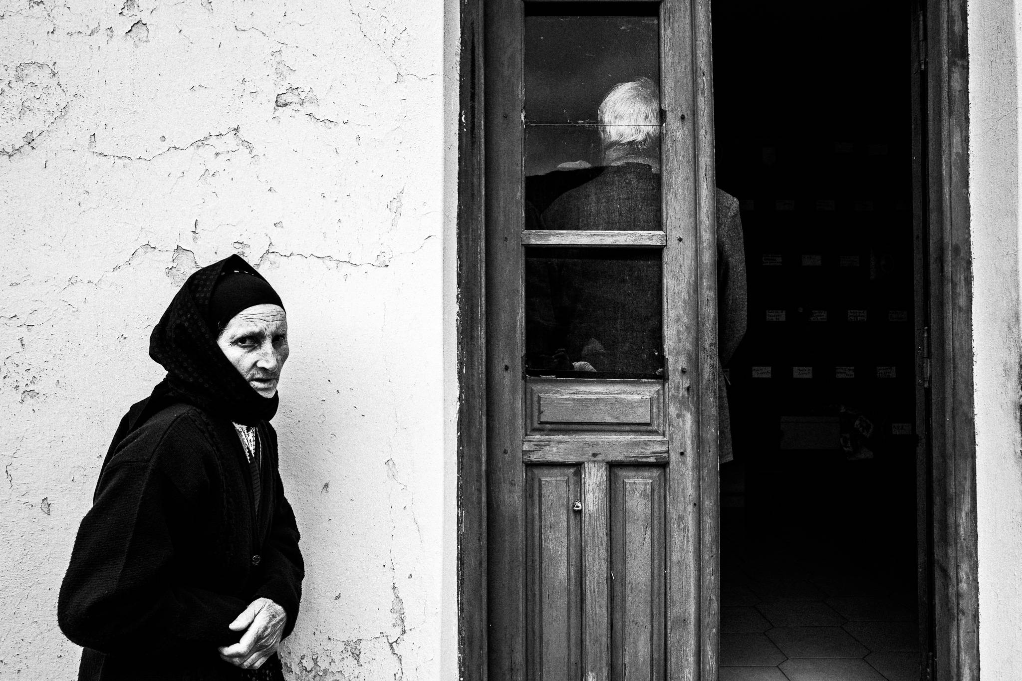 A woman in traditional black clothes, standing outside the cemetery's ossuary. Olympos, Karpathos, Greece. 