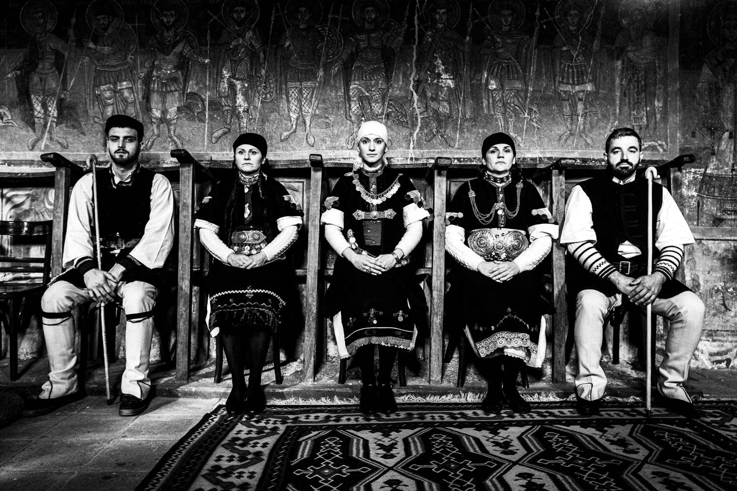 A row of five persons, sitting inside a local church. Prespes, Macedonia, Greece. Black and white photograph by George Tatakis