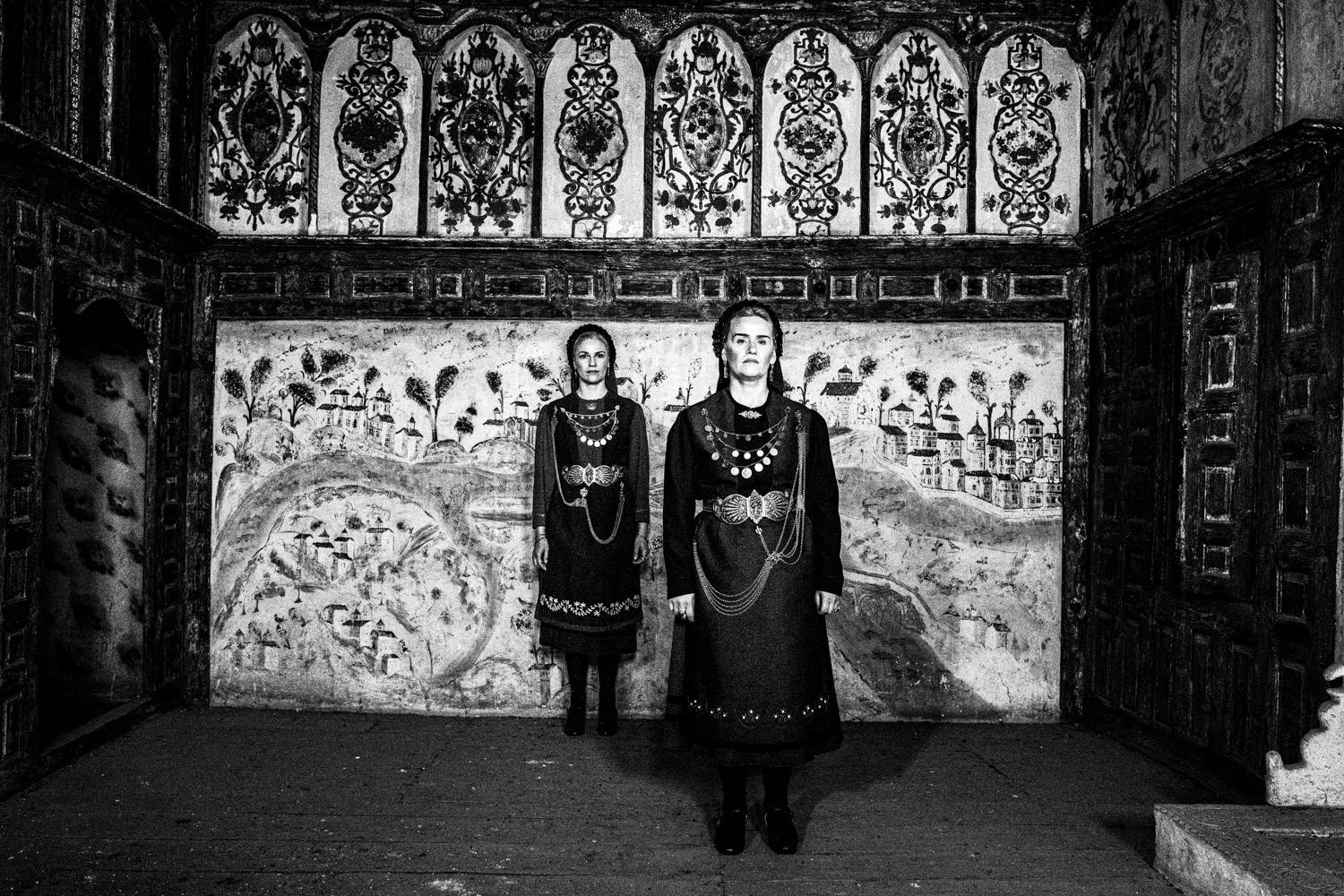 The Kamvounia dresses, against a hand painted wall in a Mansion in Siatista, Macedonia, Greece. Black and white photograph by George Tatakis