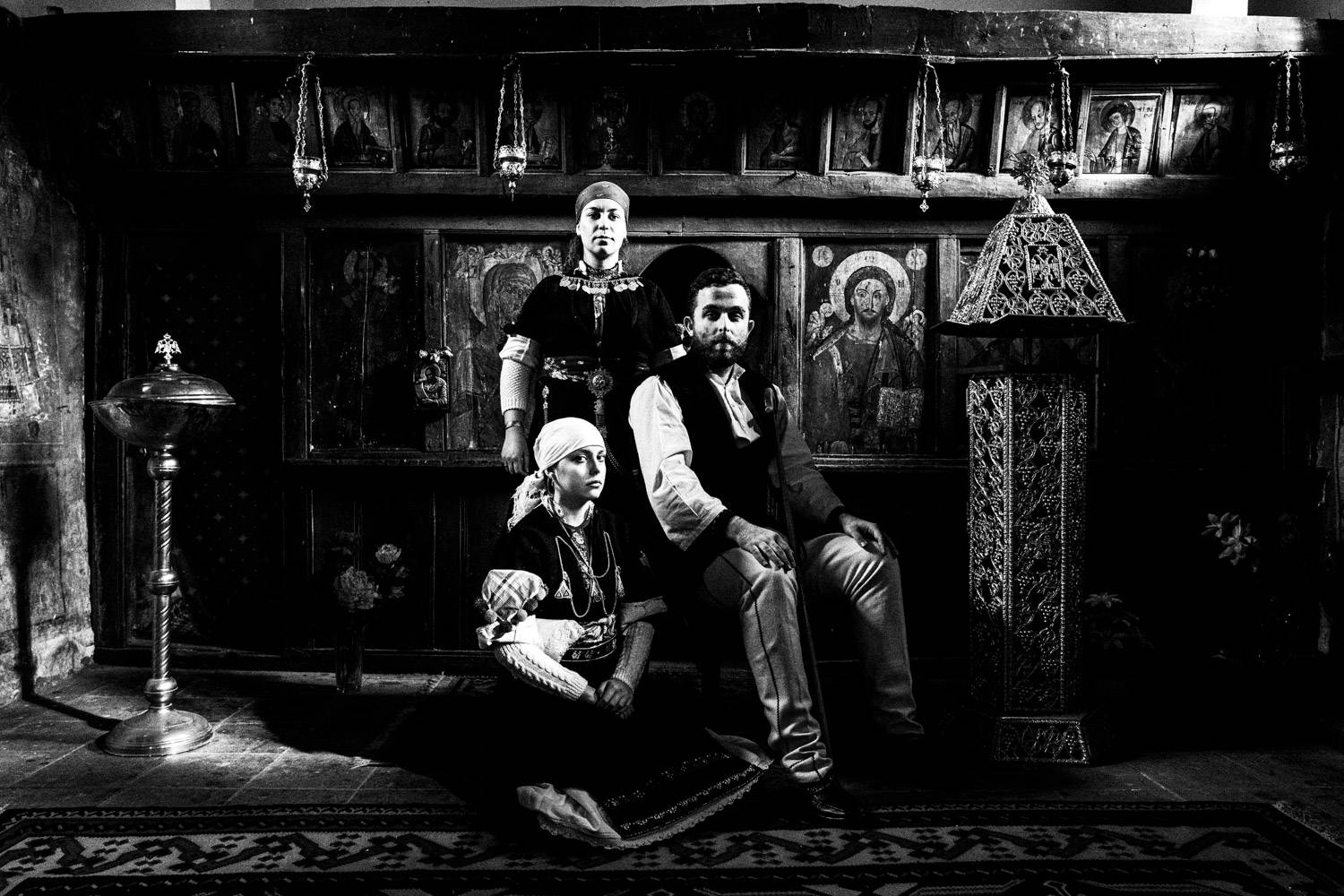A family posing inside a local church, wearing the traditional clothing. Prespes, Macedonia, Greece. Black and white photograph by George Tatakis