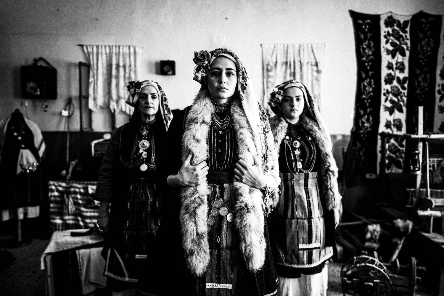 Three women posing inside the local school, wearing the traditional attire. Skopos, Florina, Macedonia, Greece. Black and white photograph by George Tatakis
