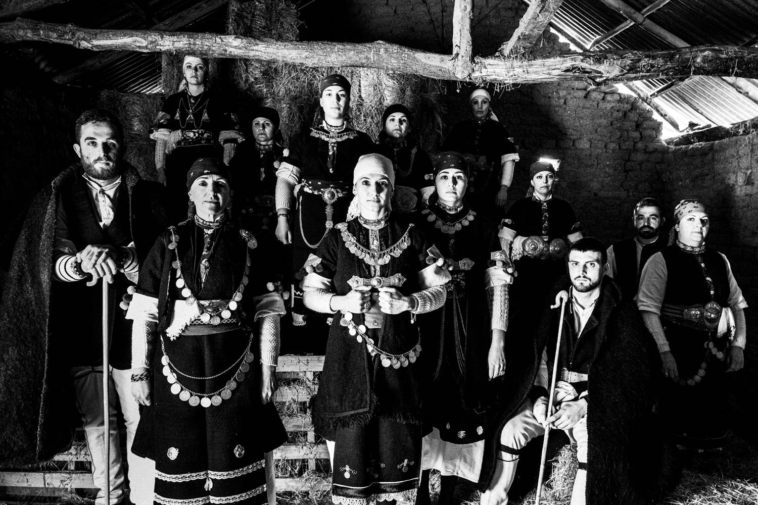 A group of 13 persons, wearing the folklore costumes of Prespes inside a local barn, Macedonia, Greece. Black and white photograph by George Tatakis