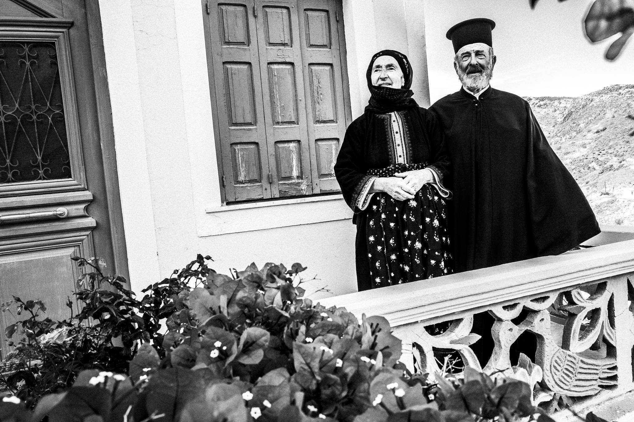 The local priest and his wife in her traditional costume, standing on their balcony. Olympos, Karpathos, Greece. 
