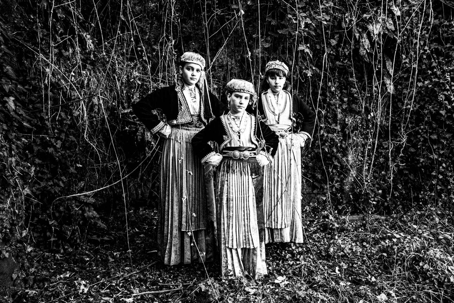 Standing portrait of three girls, in the local attire of Naoussa, Imathia, Macedonia, Greece. Black and white photograph by George Tatakis