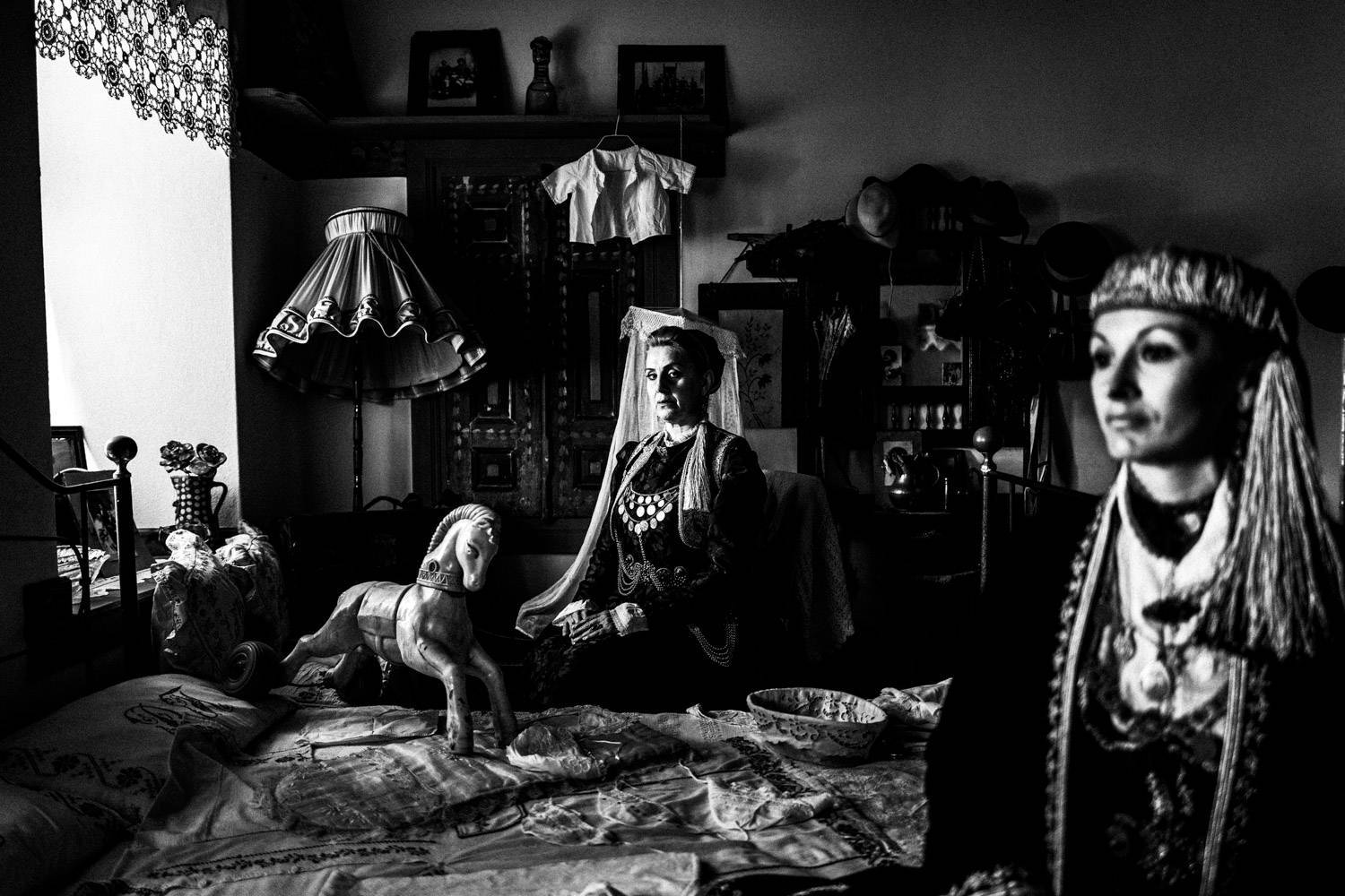 Two women sitting inside the bedroom of a traditional Mansion in Siatista, wearing the local costumes of Kozani, Macedonia, Greece. Black and white photograph by George Tatakis