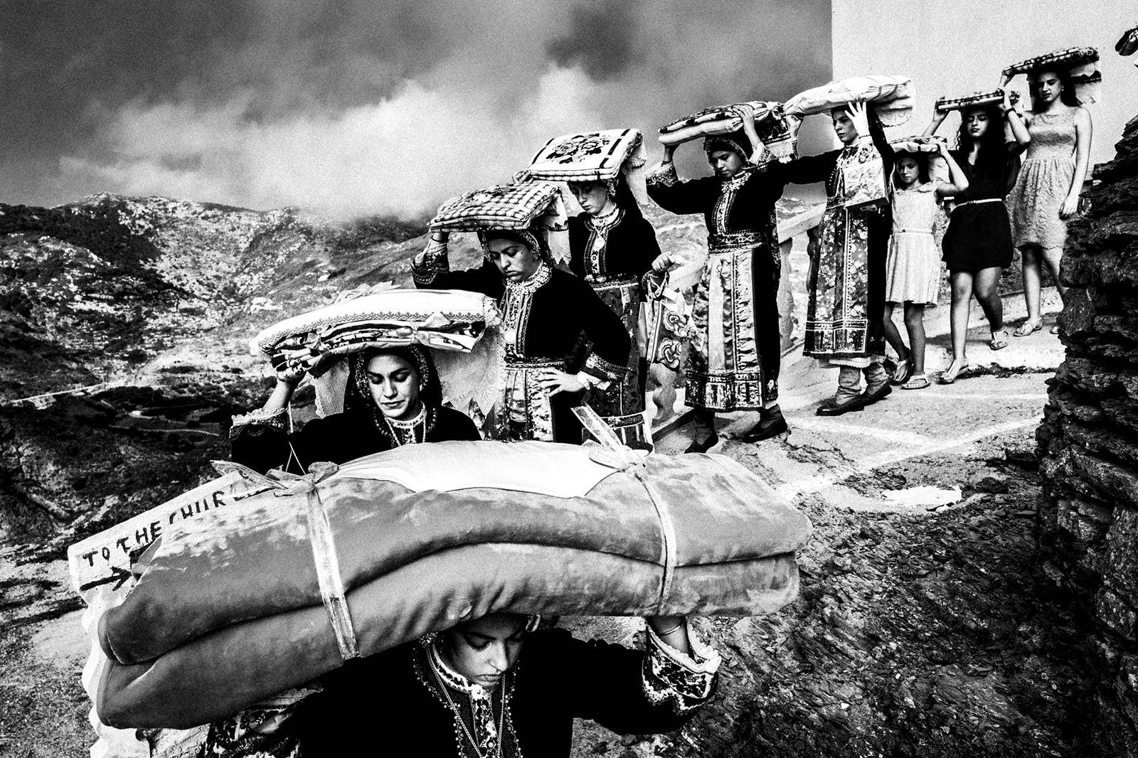 Women wearing local traditional costumes, carry the groom's dowry across the village. Olympos, Karpathos, Greece.