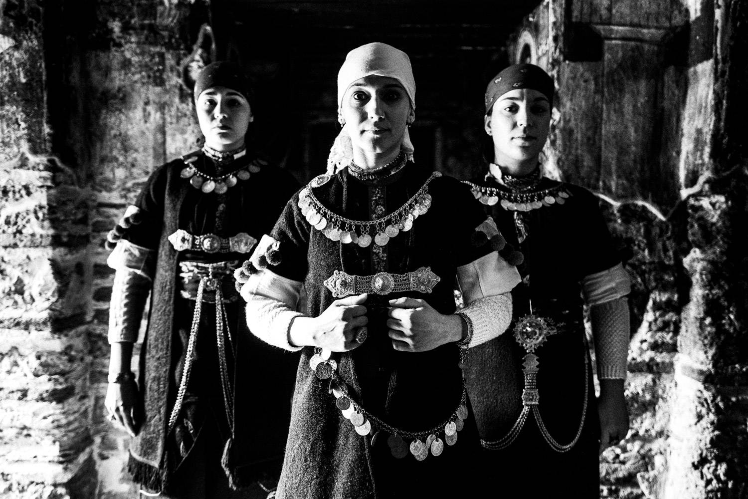 Three women inside a local church, posing in the local folklore dresses. Prespes, Macedonia, Greece. Black and white photograph by George Tatakis