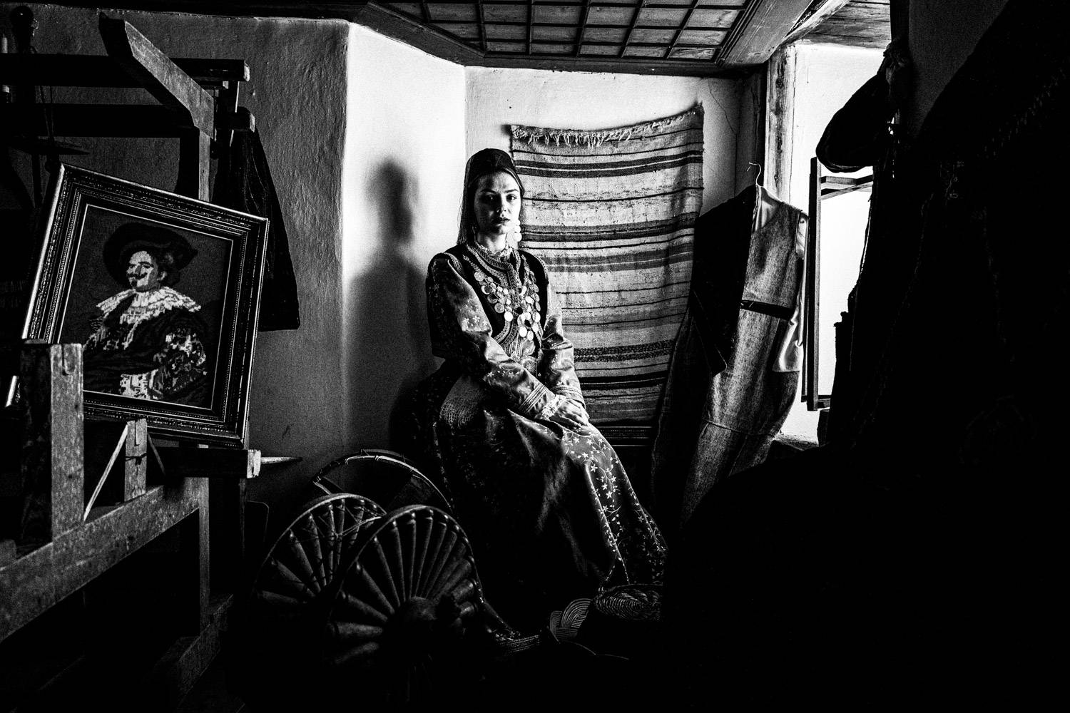 A woman in the local folklore dress, posing inside the drawing room of a traditional Mansion. Kastoria, Macedonia, Greece. Black and white photograph by George Tatakis