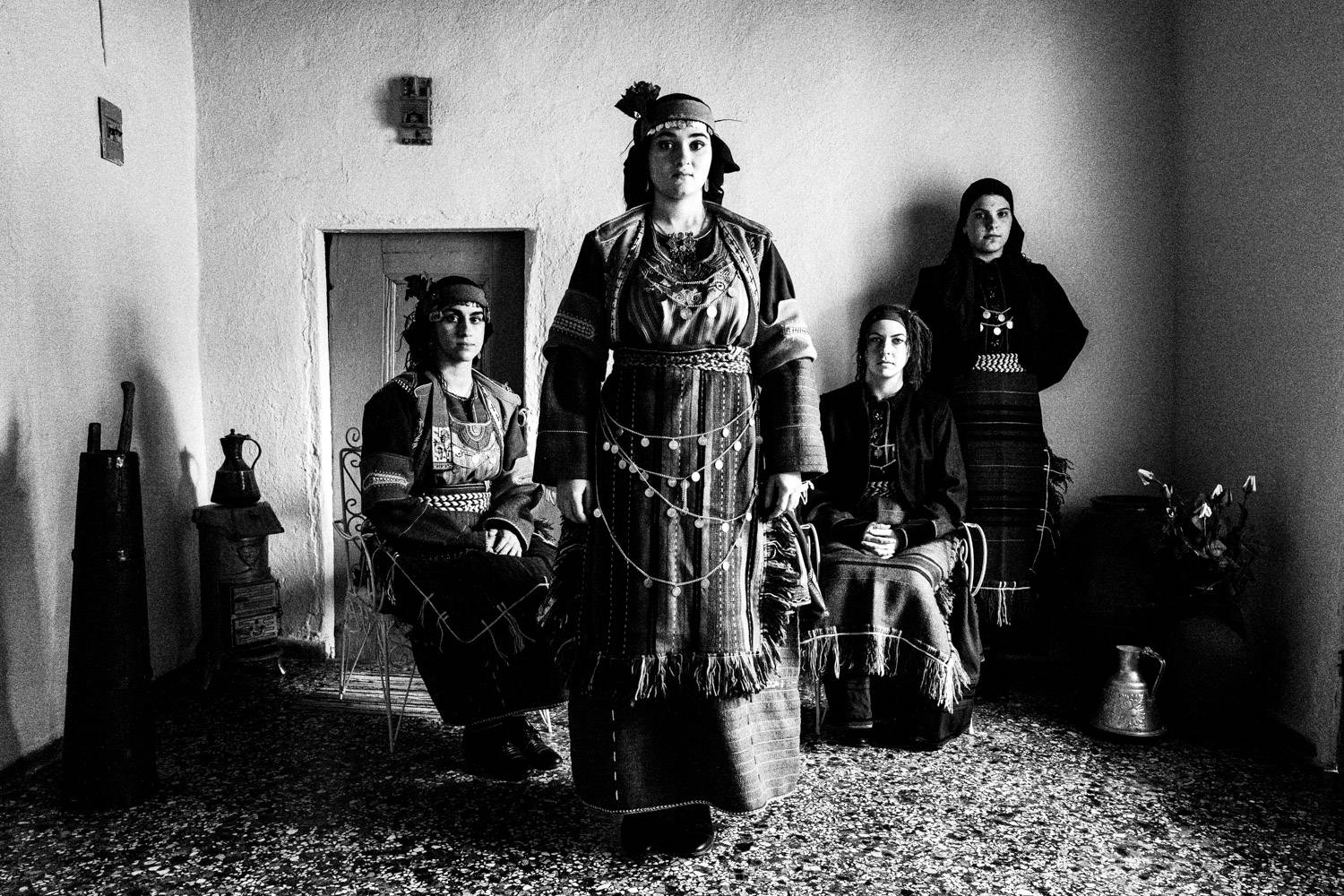Portrait of four women inside a local home, wearing the folklore dresses. Drymos, Thessaloniki, Macedonia, Greece. Black and white photograph by George Tatakis