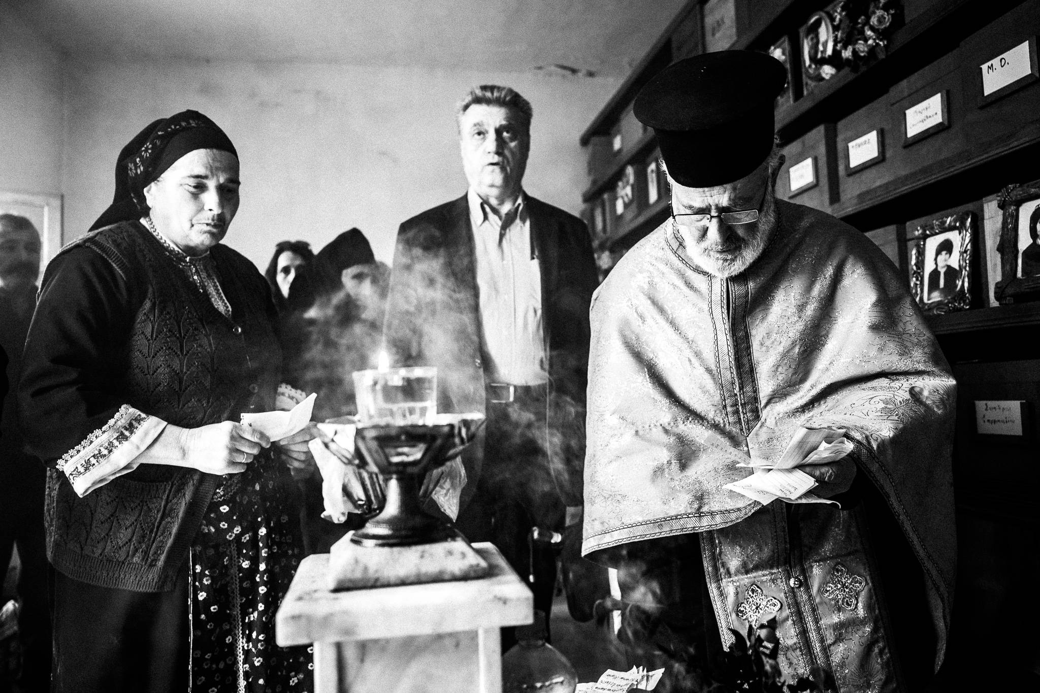 The priest with locals, performing a memorial service, inside the cemetery's ossuary. Olympos, Karpathos, Greece. 