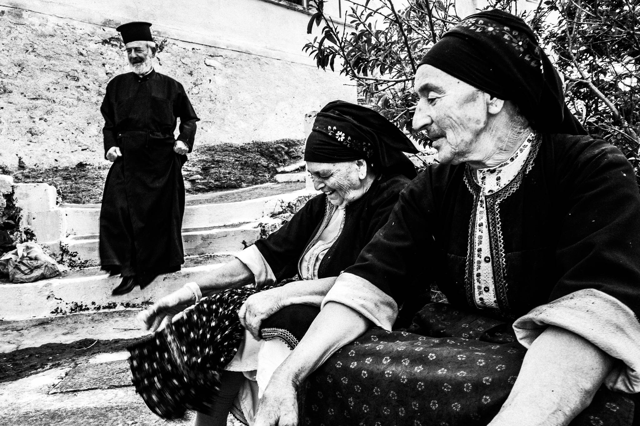 The local priest descending steps towards two elderly women in their traditional costumes. Olympos, Karpathos, Greece