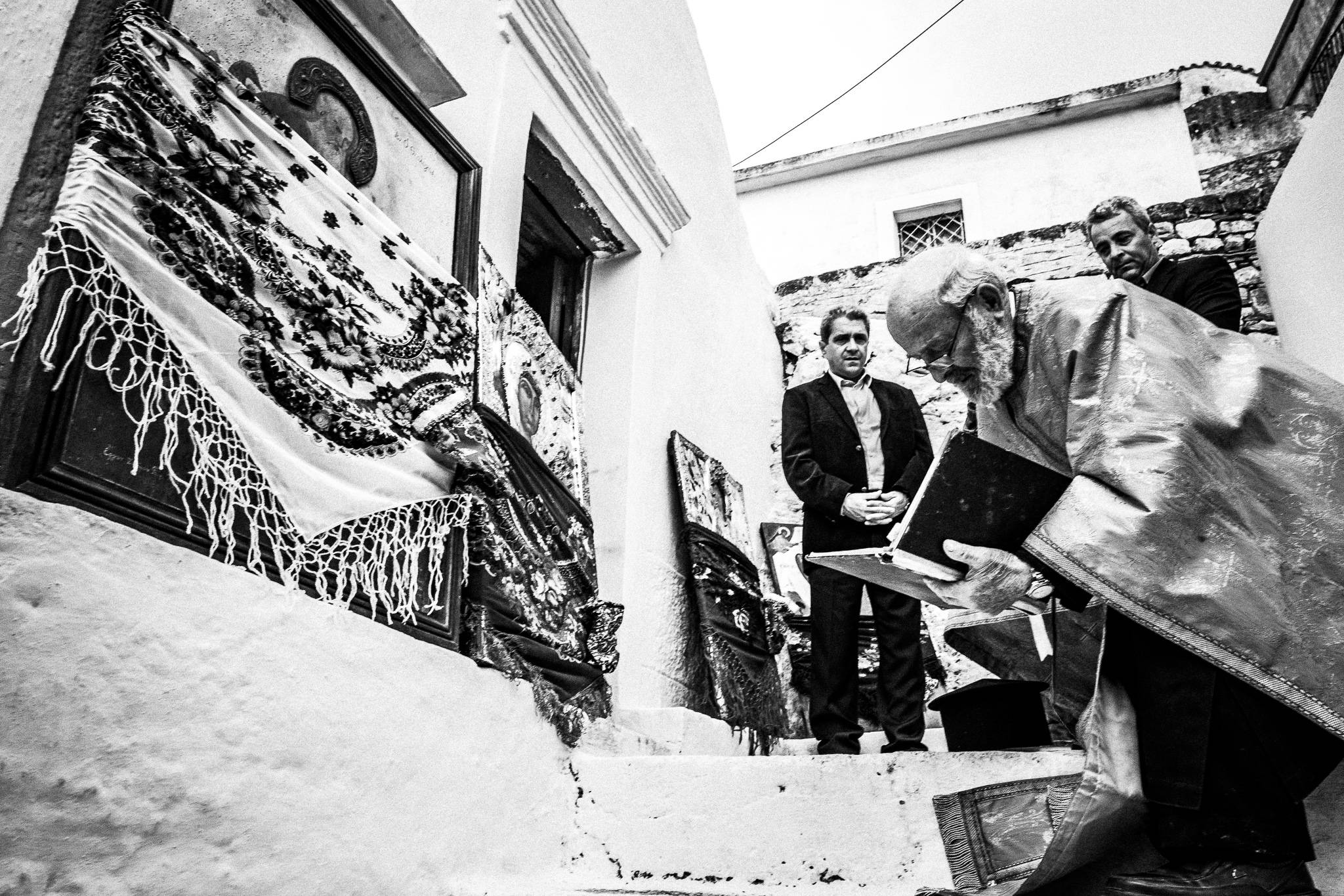 The local priest kneeling before a local church on Easter Tuesday. Olympos, Karpathos, Greece. 