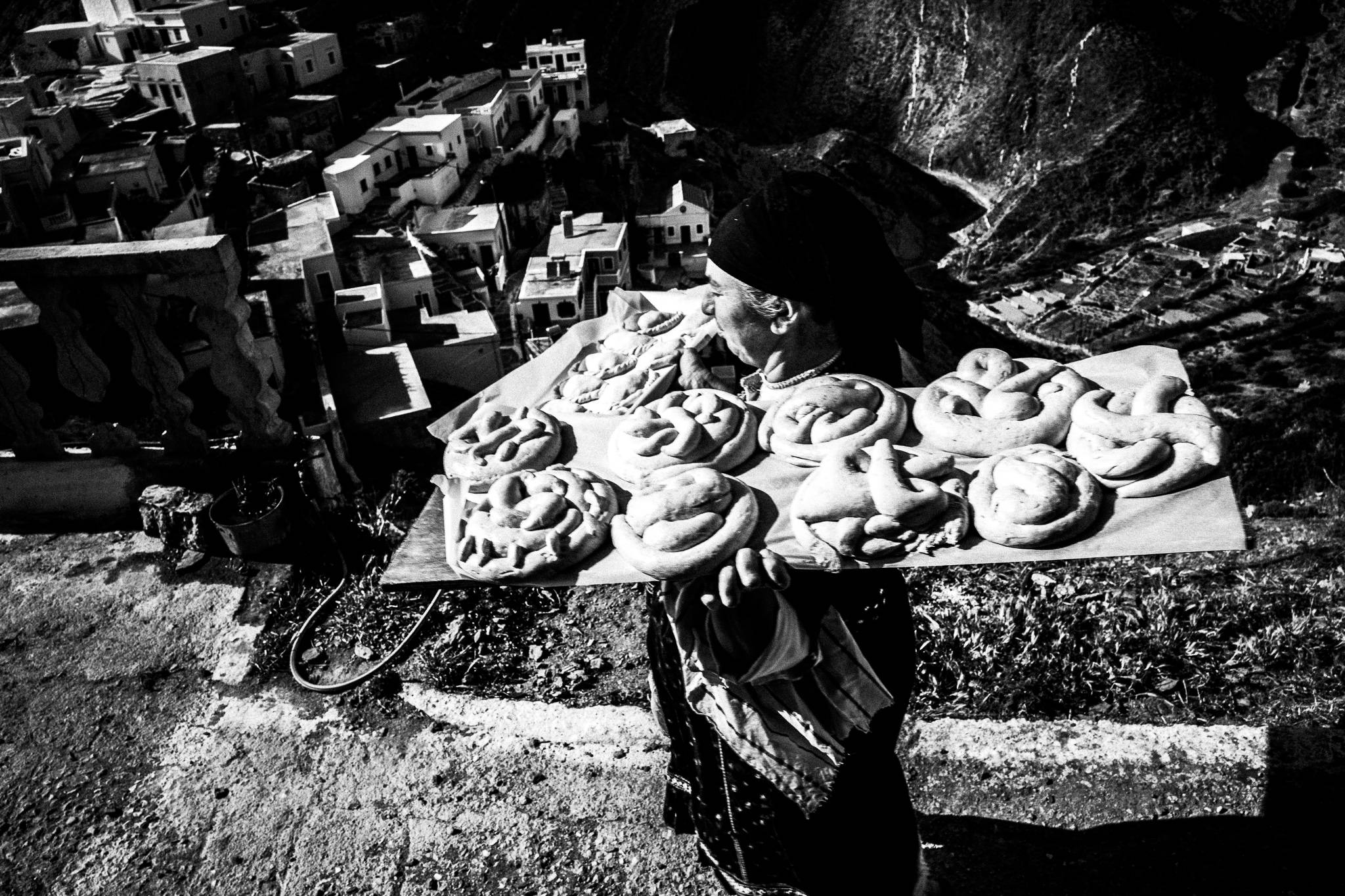 A woman in the traditional costume, carrying two trays of Easter bread across an alley in Olympos, Karpathos, Greece