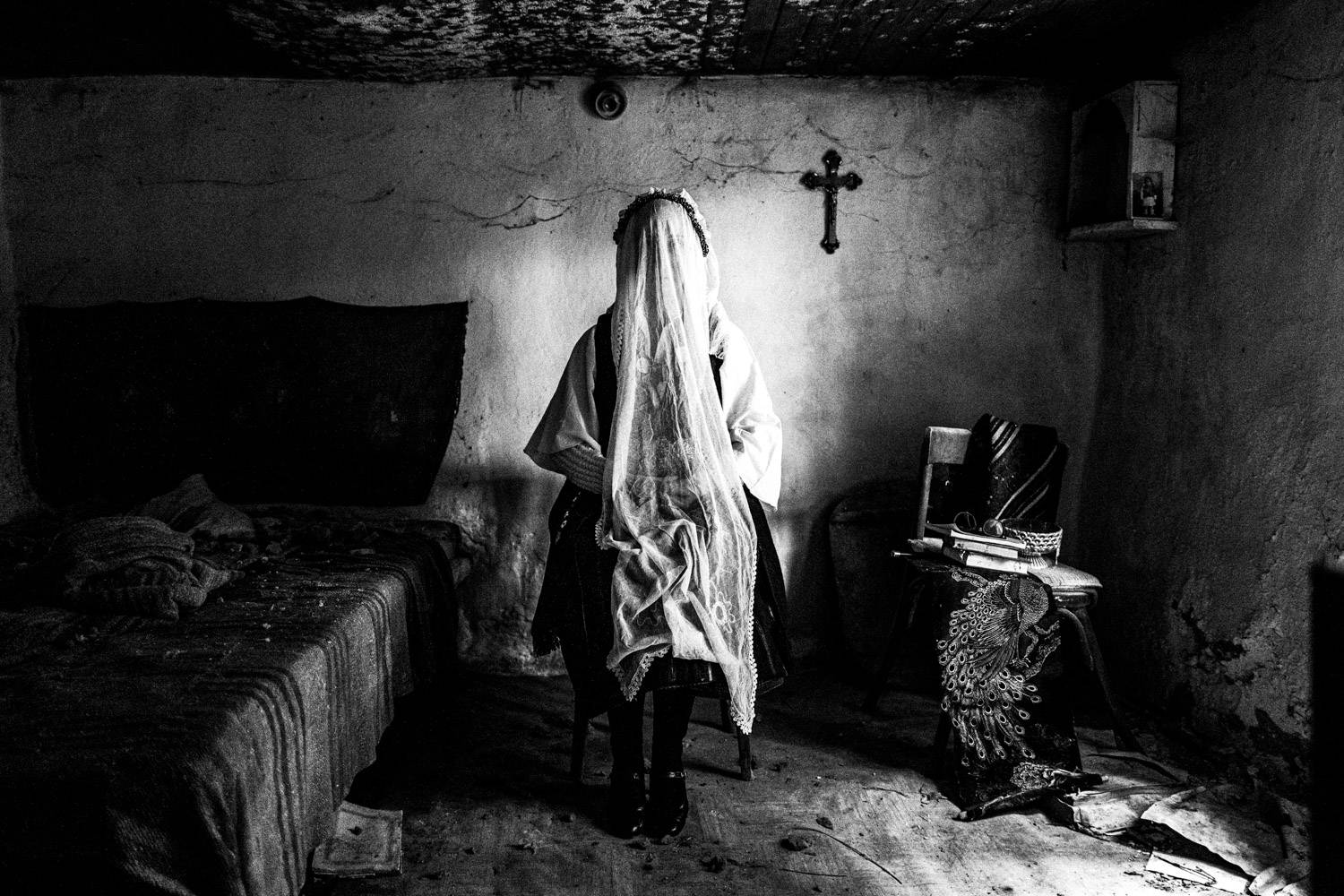Sitting portrait of a veiled bride in the folklore dress, inside a local abandoned house. Ermakia, Ptolemaida, Macedonia, Greece. Black and white photograph by George Tatakis