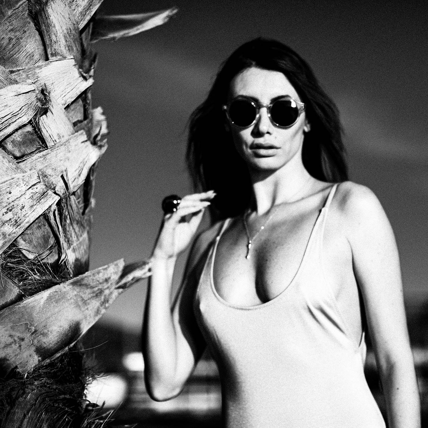 Black and white photograph of a professional model posing next to a palm tree