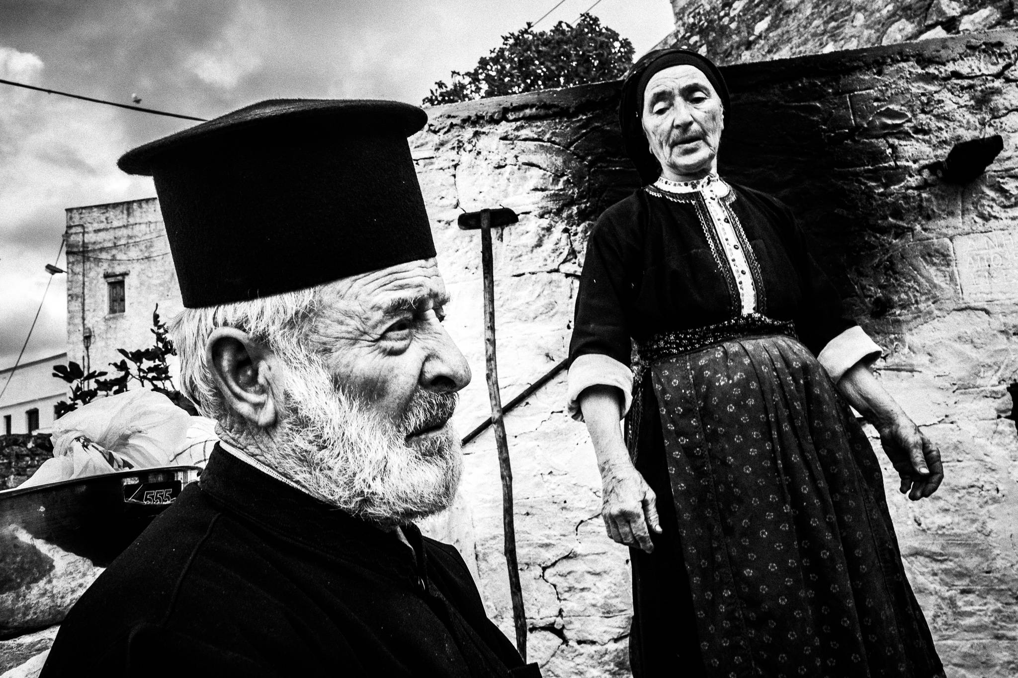 The local priest and his wife in her traditional costume, outside the local wood-burning oven. Olympos, Karpathos, Greece