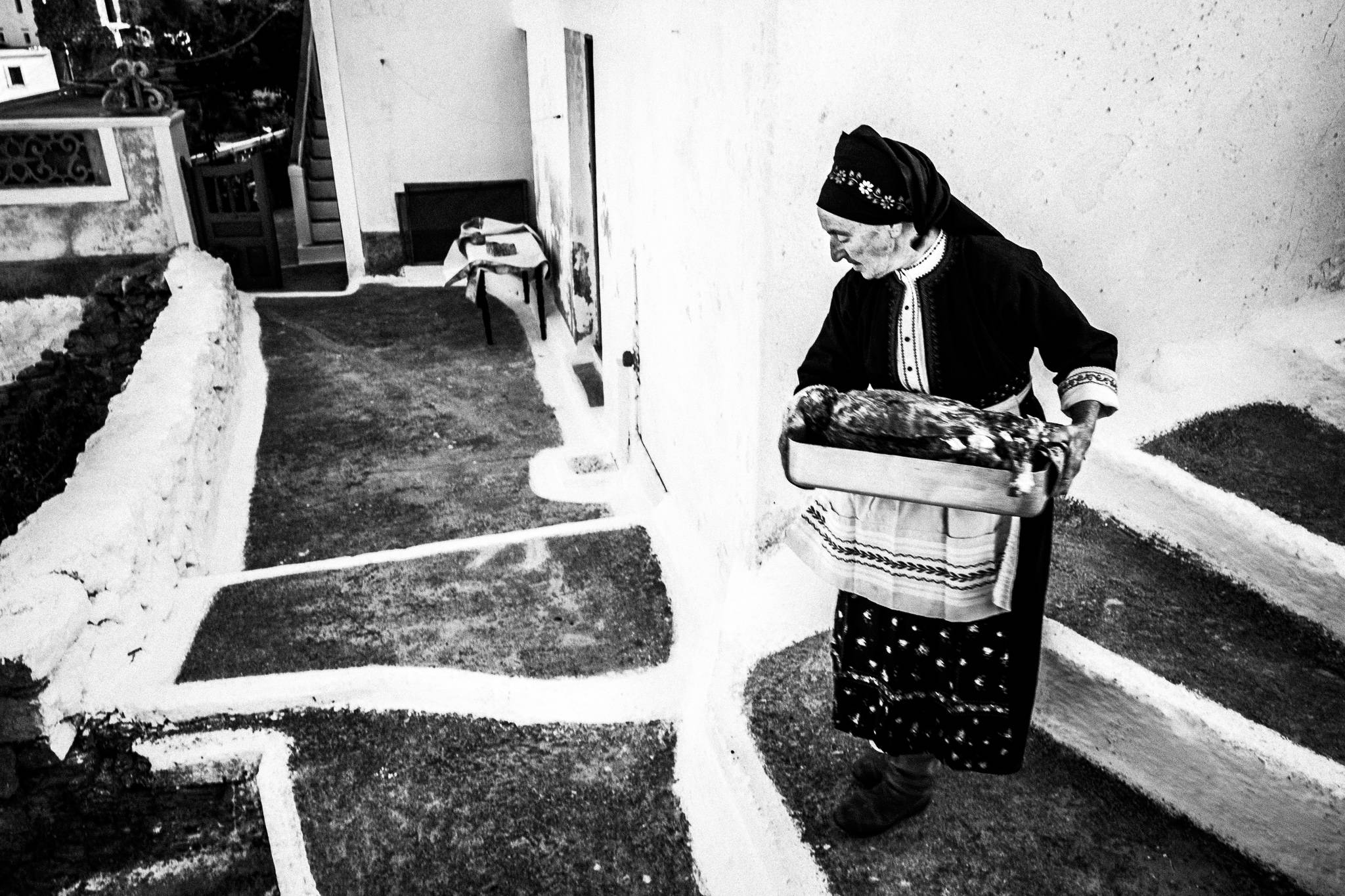 An elderly woman in her traditional attire, bringing a tray with the goat to the wood-burning oven. Olympos, Karpathos, Greece. 
