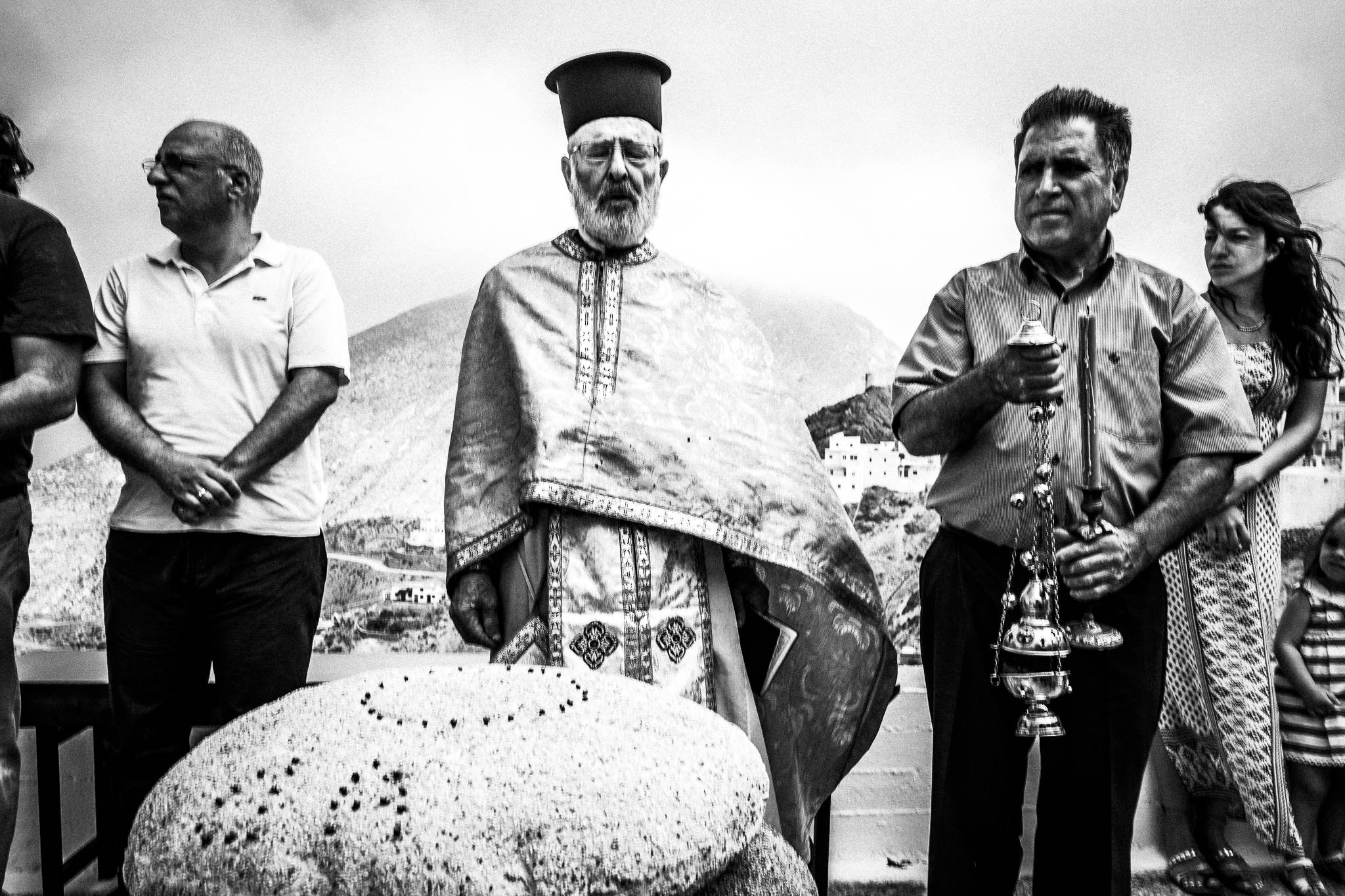 Papa-Yannis blessing the bread, made by local women. The Transfiguration of the Saviour in Olympos, Karpathos, Greece. Black and white photography by George Tatakis