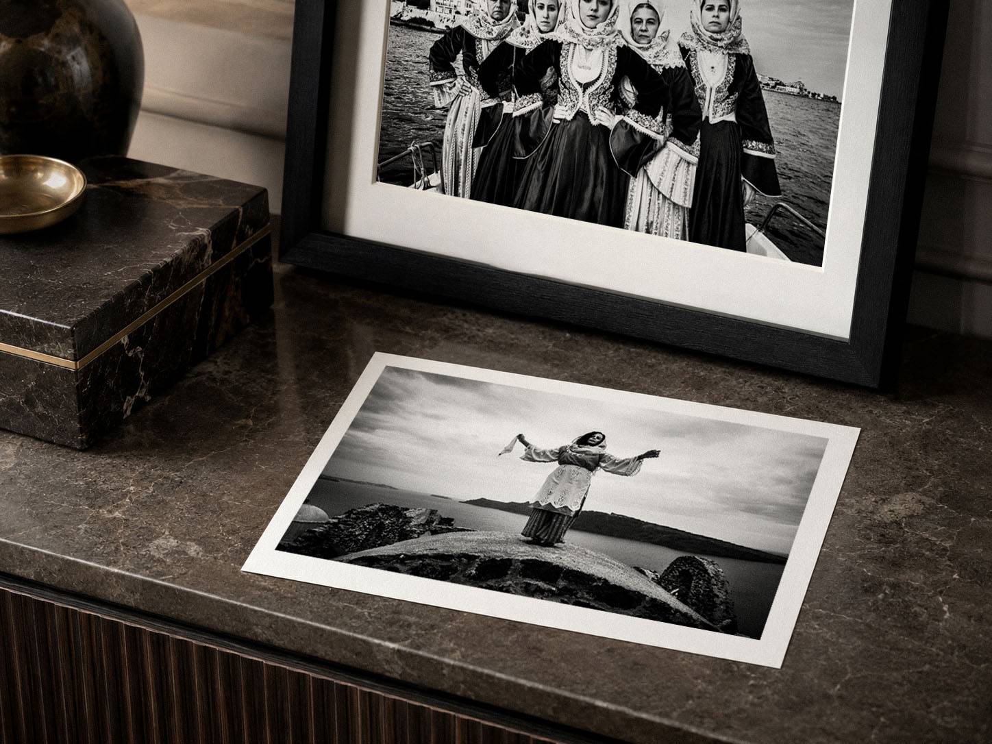 Black-and-white fine-art photography prints shown with a framed Caryatis work and an unframed landscape print on a dark marble surface.