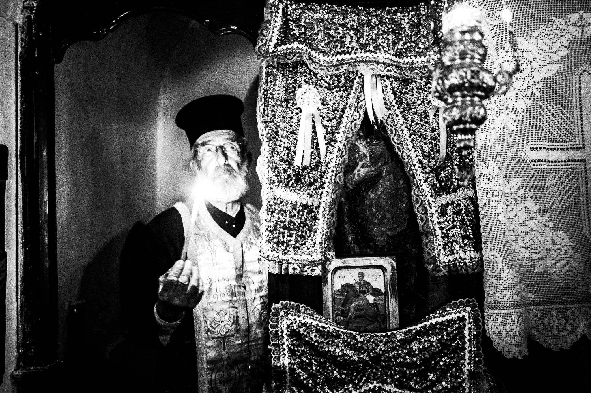 Papa Yannis inside the church of St. Minas as he performs a christening, Olympos, Karpathos, Greece. Black and white photography by George Tatakis