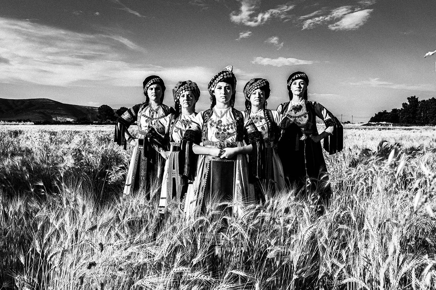 A group of women in a wheat field, wearing the traditional Karagouna clothes of Trikala, Thessaly, Greece. Black and white photography by George Tatakis