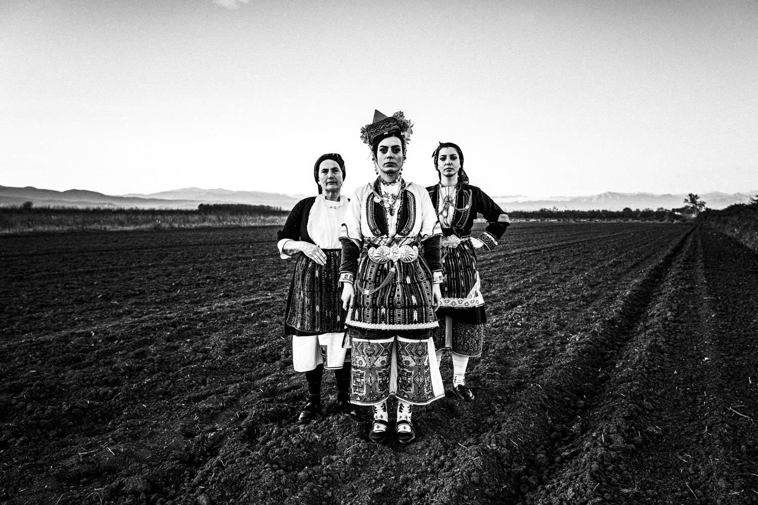 Three women at a local field, wearing the traditional costumes. Aggelochori, Naoussa, Macedonia, Greece. Black and white photograph by George Tatakis