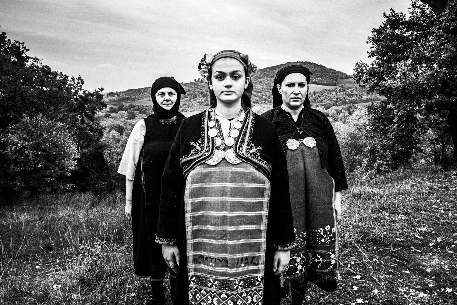 Three women posing, wearing the Kostellides attire in the local mountains. Meliki, Imathia, Macedonia, Greece. Black and white photograph by George Tatakis