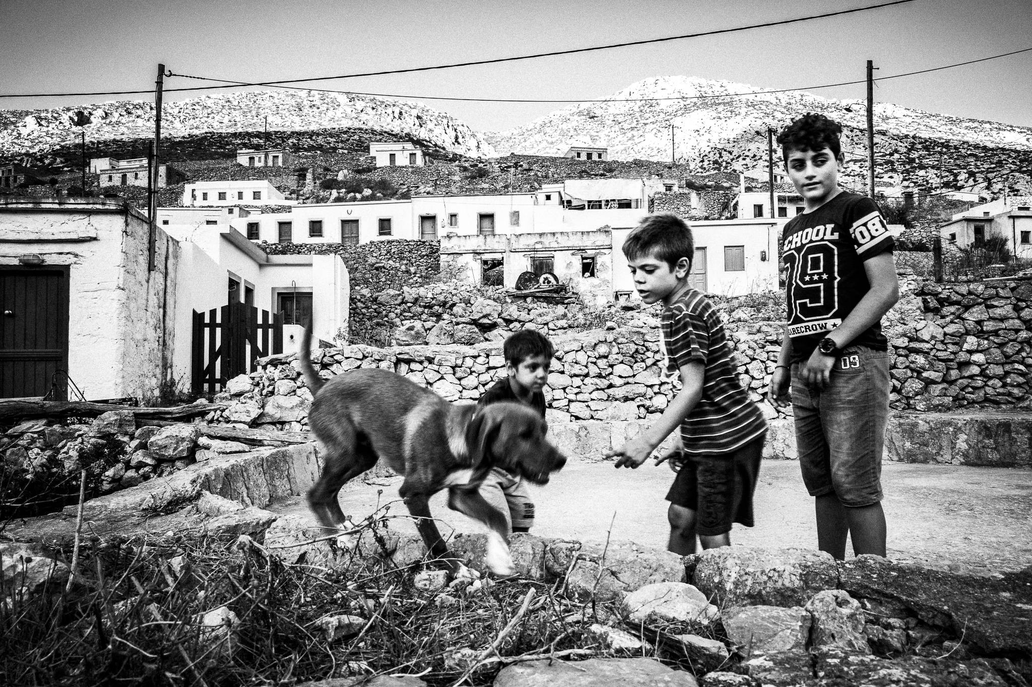 Children playing at Avlona with a stray dog. Olympos, Karpathos, Greece. Black and white photography by George Tatakis