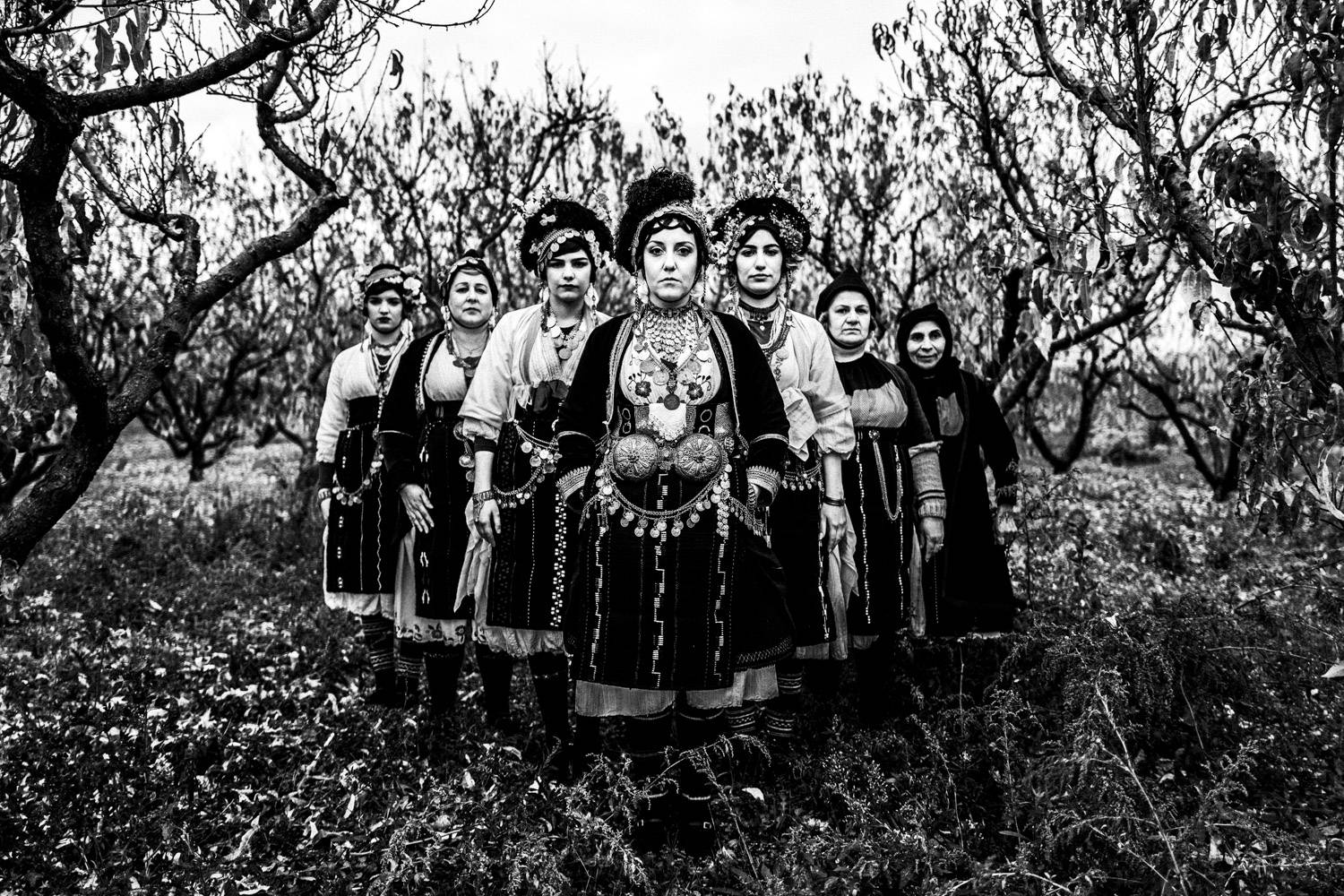 A group of women wearing the Roumlouki costume, amidst a local pistachio farm. Meliki, Imathia, Macedonia, Greece. Black and white photograph by George Tatakis