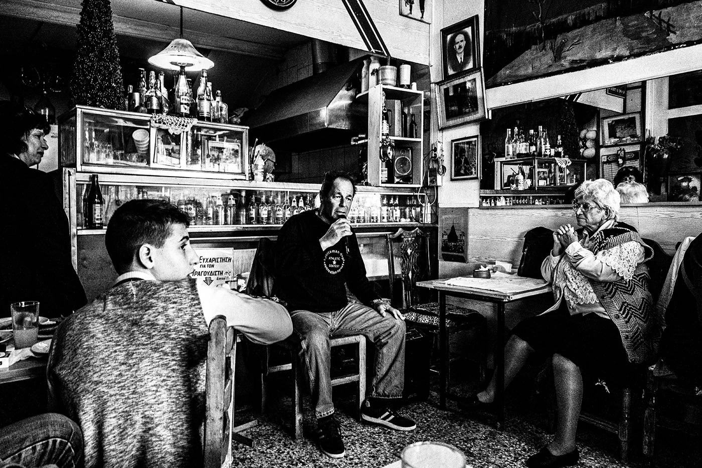 Ο τραγουδιστής στο καφενείο Θεόκλητος - Ένα κρυμμένο στολίδι στον Πειραιά, Ελλάδα. Ασπρόμαυρη φωτογραφία του Γιώργου Τατάκη
