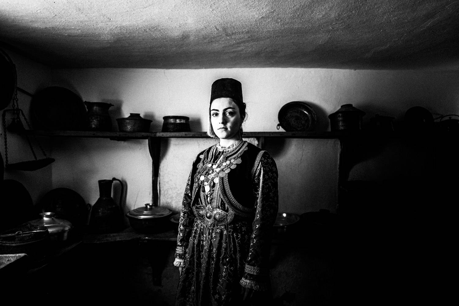 A woman wearing the local traditional attire inside the kitchen of a traditional Mansion. Kastoria, Macedonia, Greece. Black and white photograph by George Tatakis