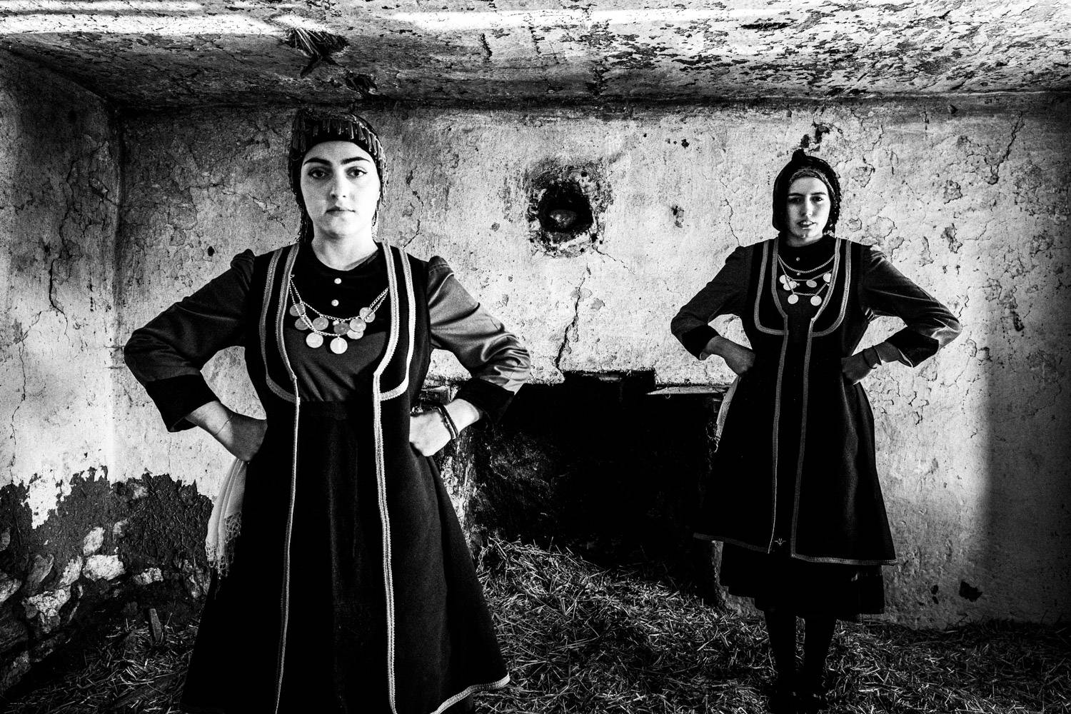 Two women posing in the local rural costume inside an old house. Lefki, Kastoria, Macedonia, Greece. Black and white photograph by George Tatakis