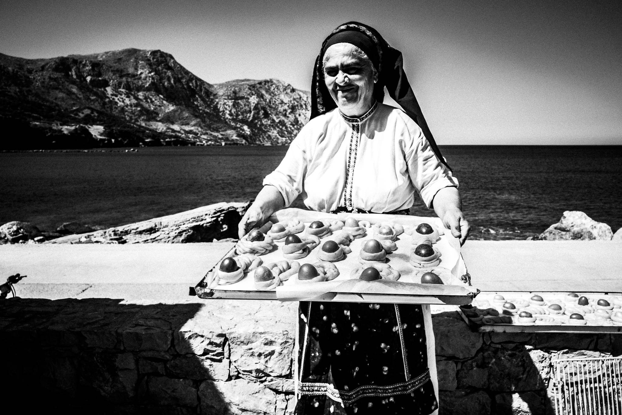 A woman by the harbor, in her traditional clothes, carrying a tray of 'Pouloi', the Easter bread. Diafani, Karpathos, Greece