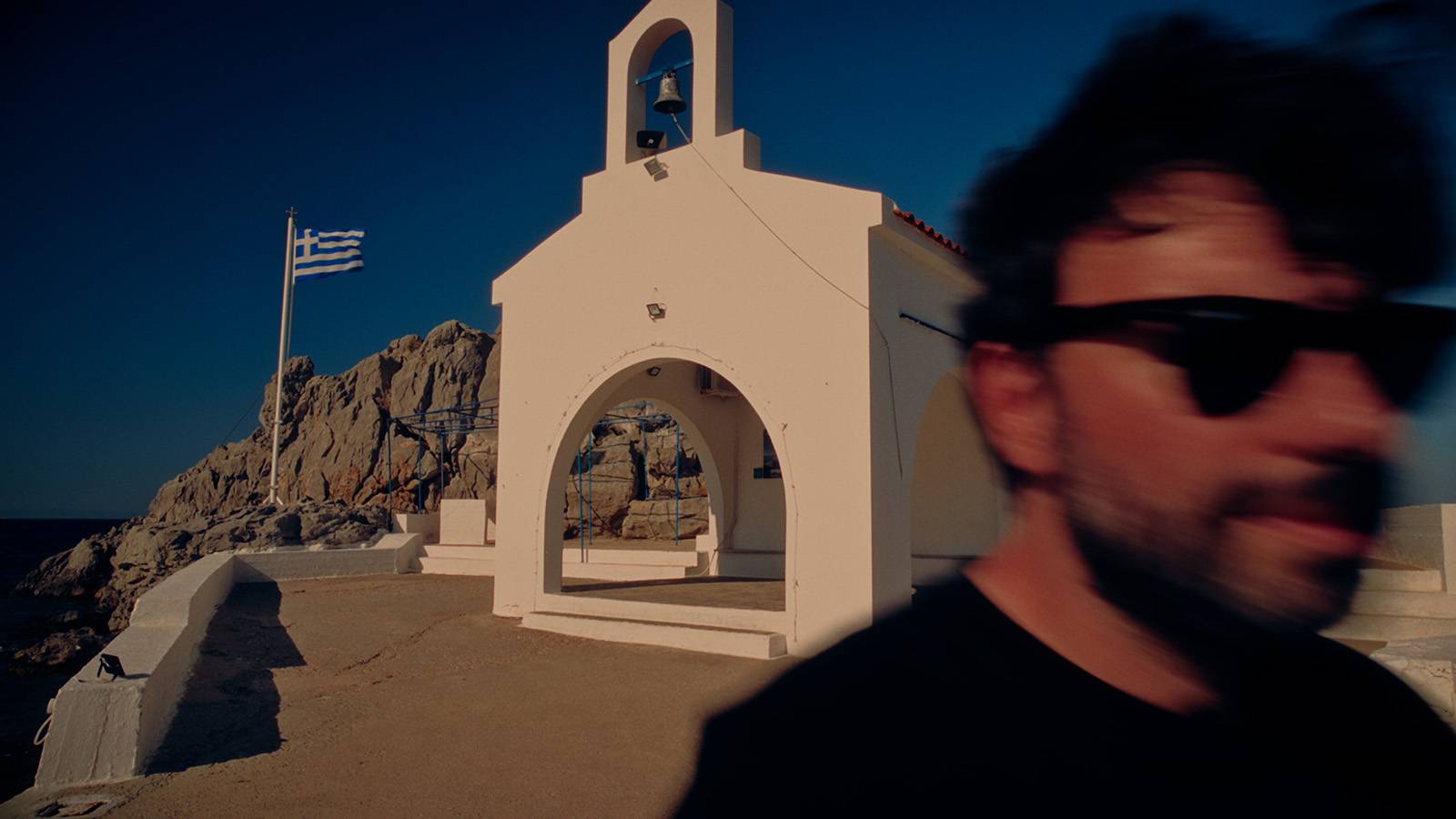 George Tatakis passing in front of the white seaside chapel of Agios Isidoros in Chios.