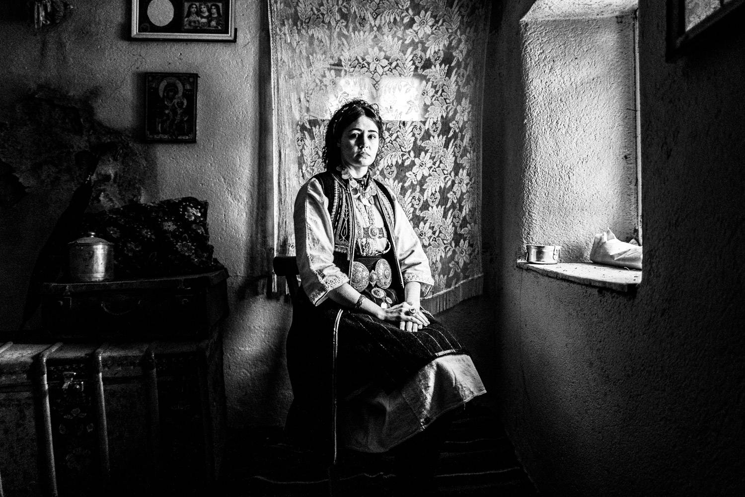 Sitting portrait of a woman inside a local traditional home, wearing the traditional costume.  Polypotamos, Florina, Macedonia, Greece. Black and white photograph by George Tatakis