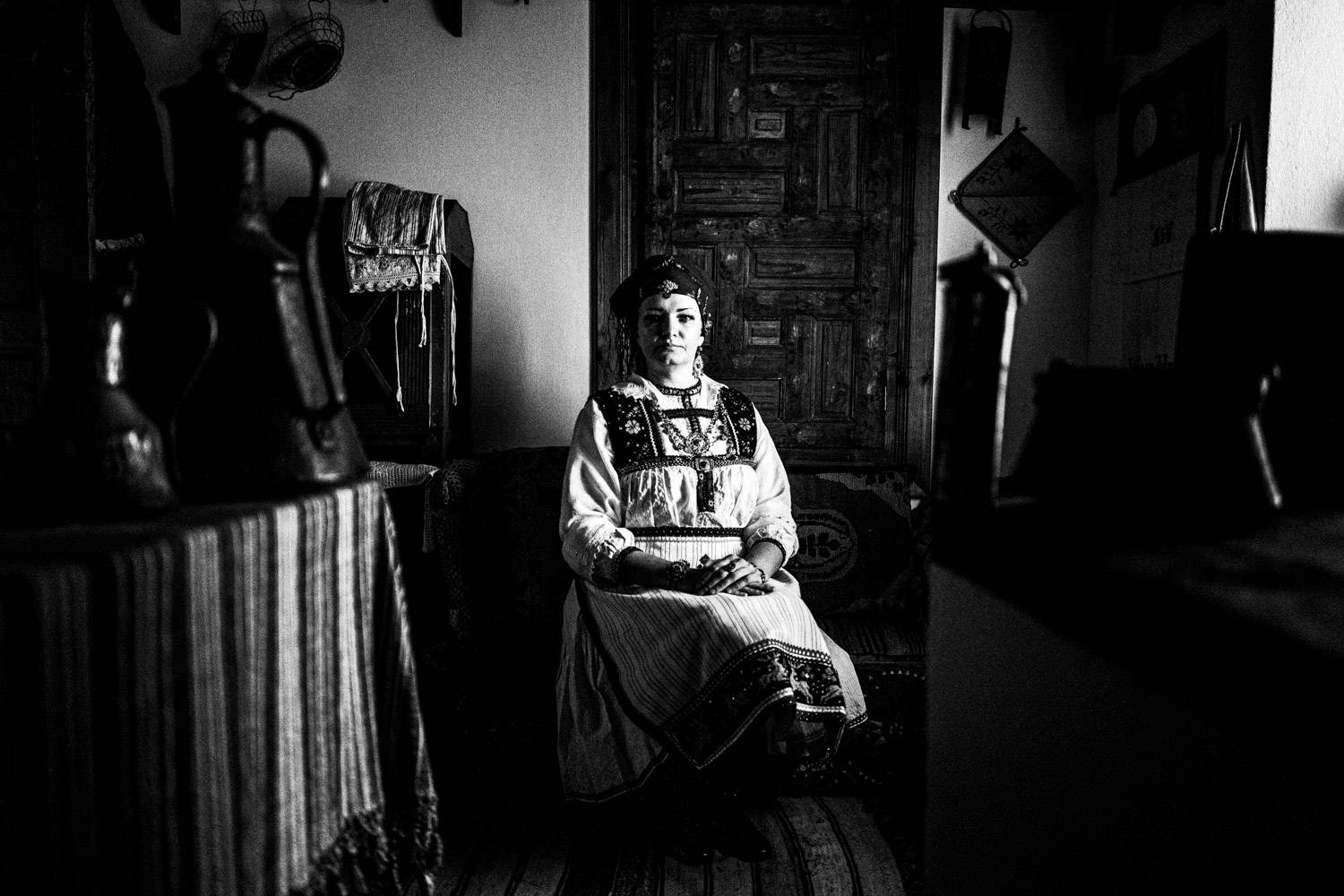 Sitting portrait of a woman inside the kitchen of a Mansion in Siatista, wearing the folklore dress of Tsartsampas. Macedonia, Greece. Black and white photograph by George Tatakis