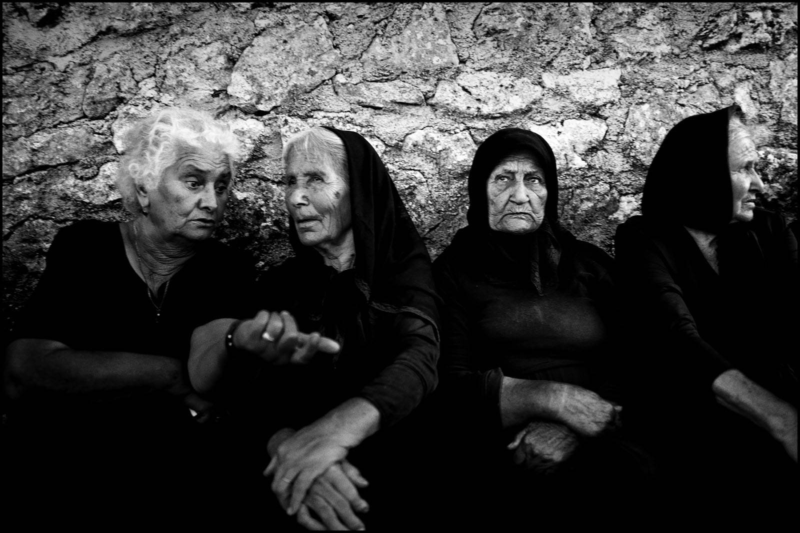 Women chatting outside a church in traditional Greek clothing. Egglouvi, Lefkada, Greece.