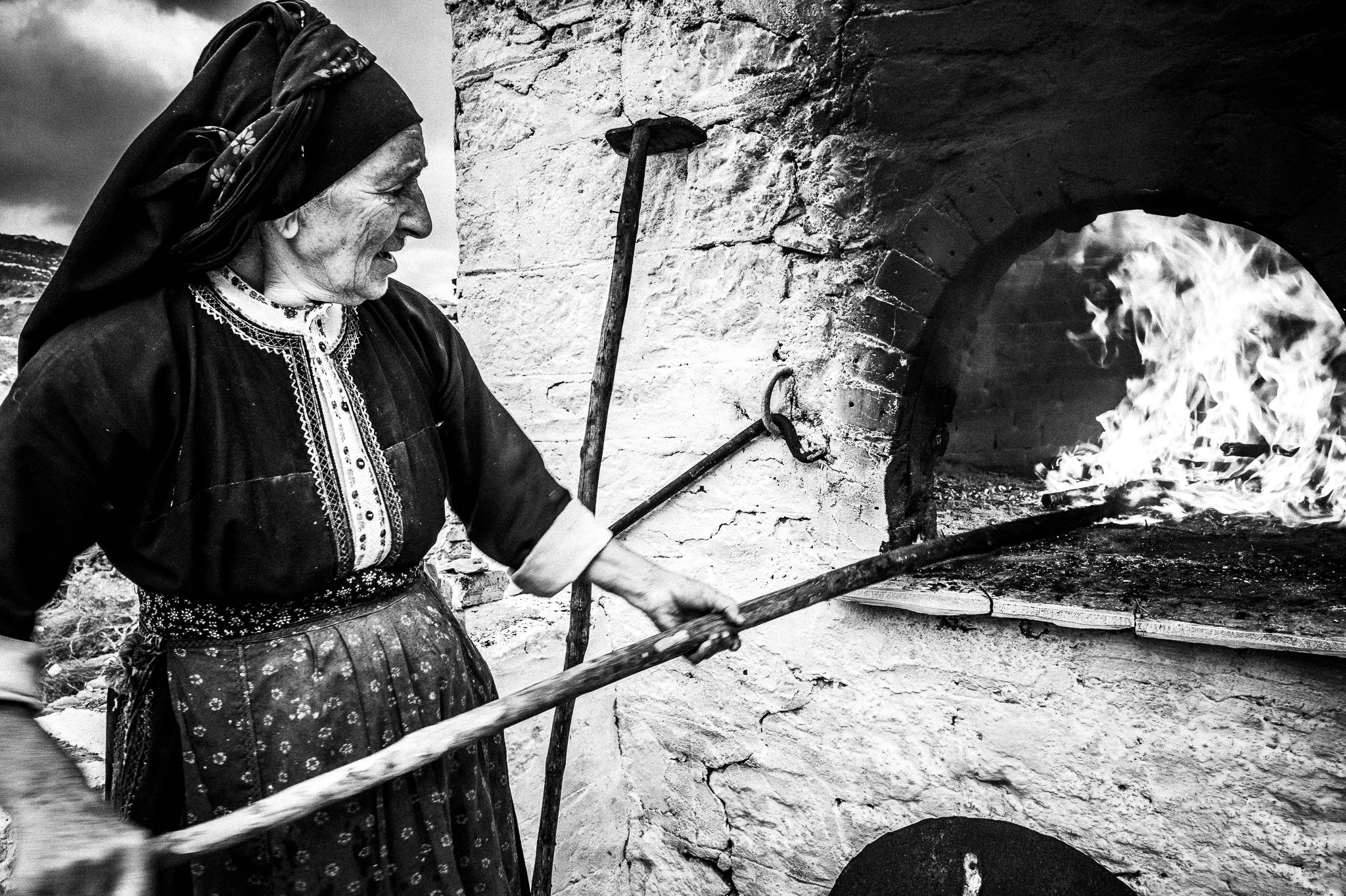 An elderly woman in the local traditional costume, lighting up the wood burning oven in Olympos, Karpathos, Greece