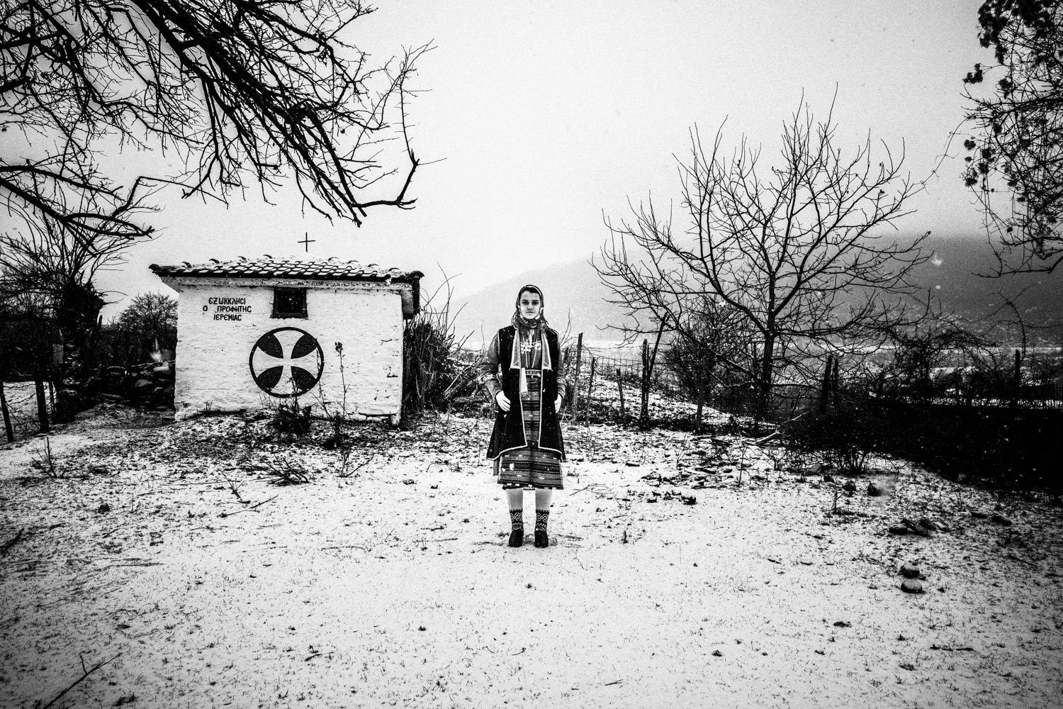 Portrait of a woman in the snow next to a chapel in Volax, Macedonia, Greece. Black and white photograph by George Tatakis