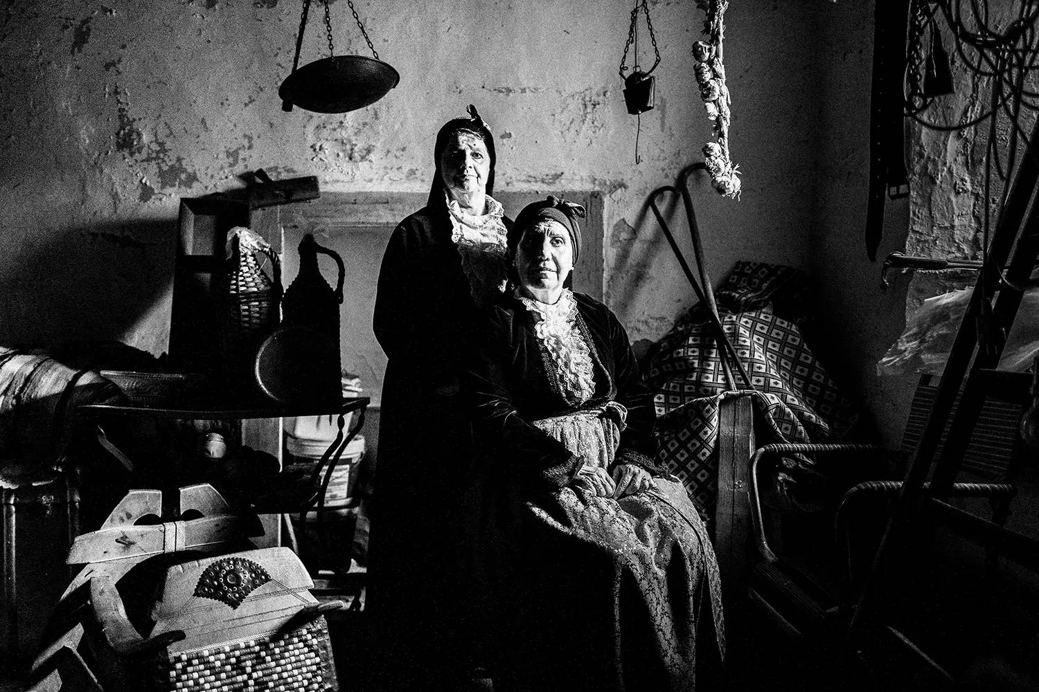 Δύο ηλικιωμένες γυναίκες μέσα σε μια εγκαταλελειμμένη αποθήκη στην Πορταριά, φορώντας τις παραδοσιακές φορεσιές του Πηλίου, Θεσσαλία, Ελλάδα. Ασπρόμαυρη φωτογραφία του Γιώργου Τατάκη