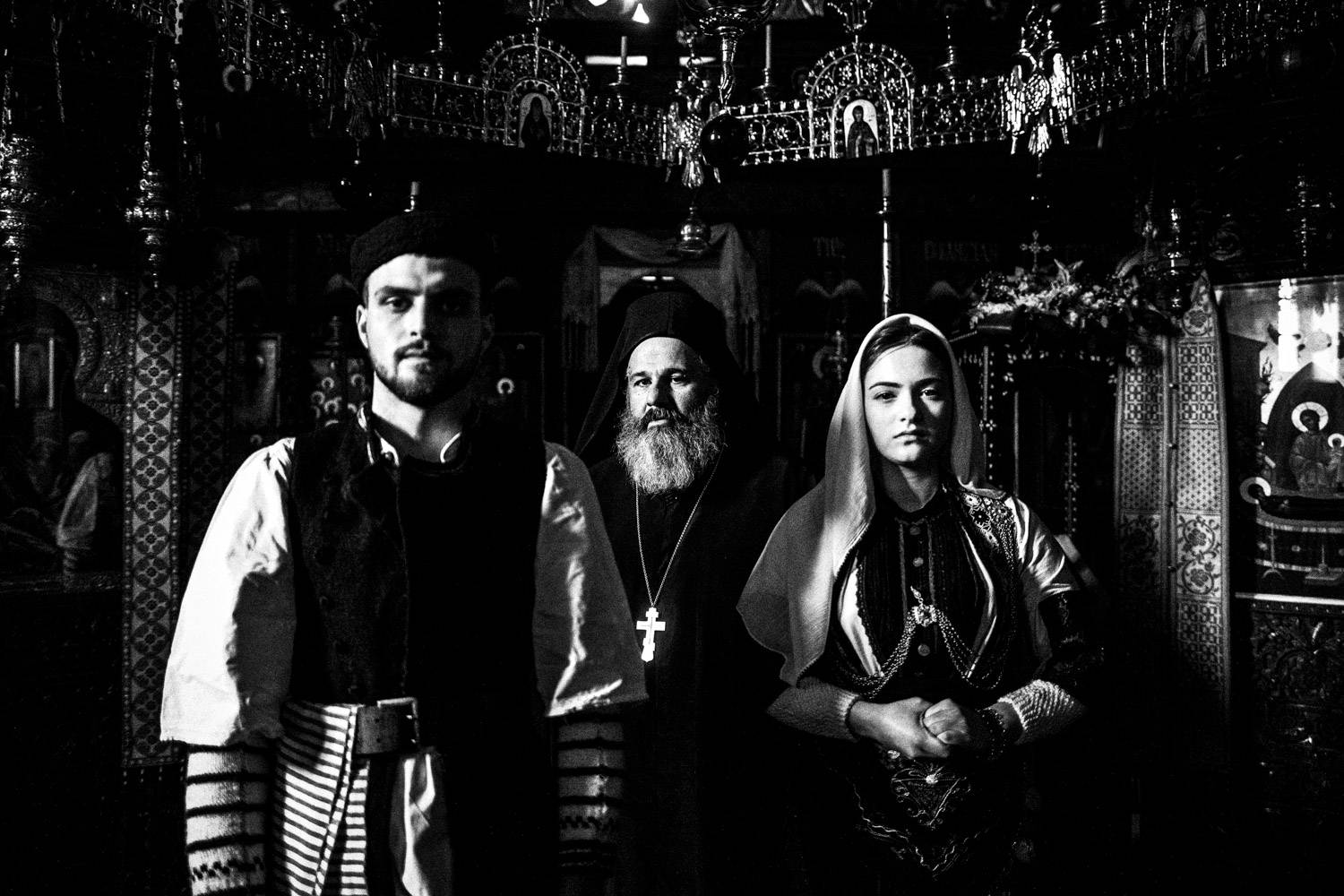 A priest with a couple dressed in the local attire at the local Monastery's church. Kladorachi, Florina, Macedonia, Greece. Black and white photograph by George Tatakis