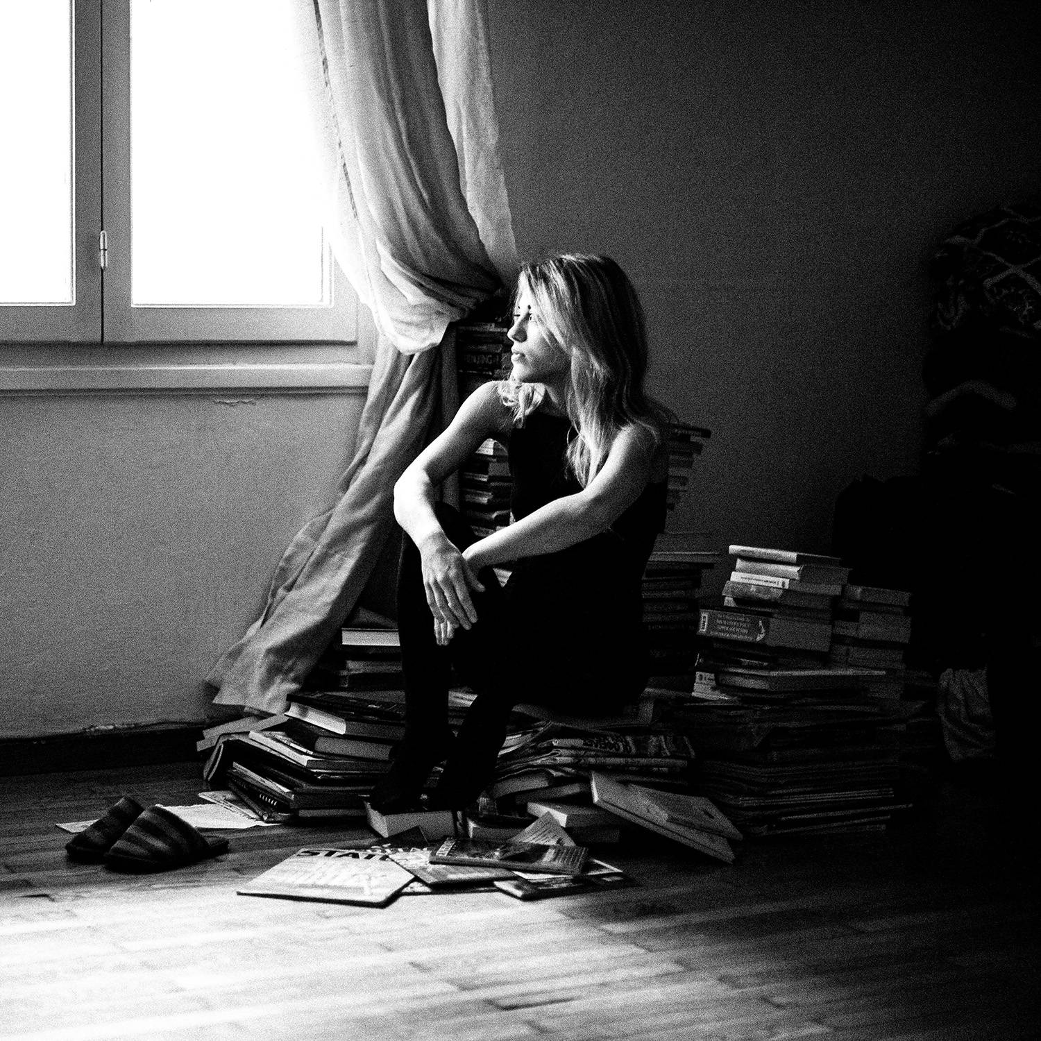 Black and white photograph of an actress posing by sitting on top of a pile of books