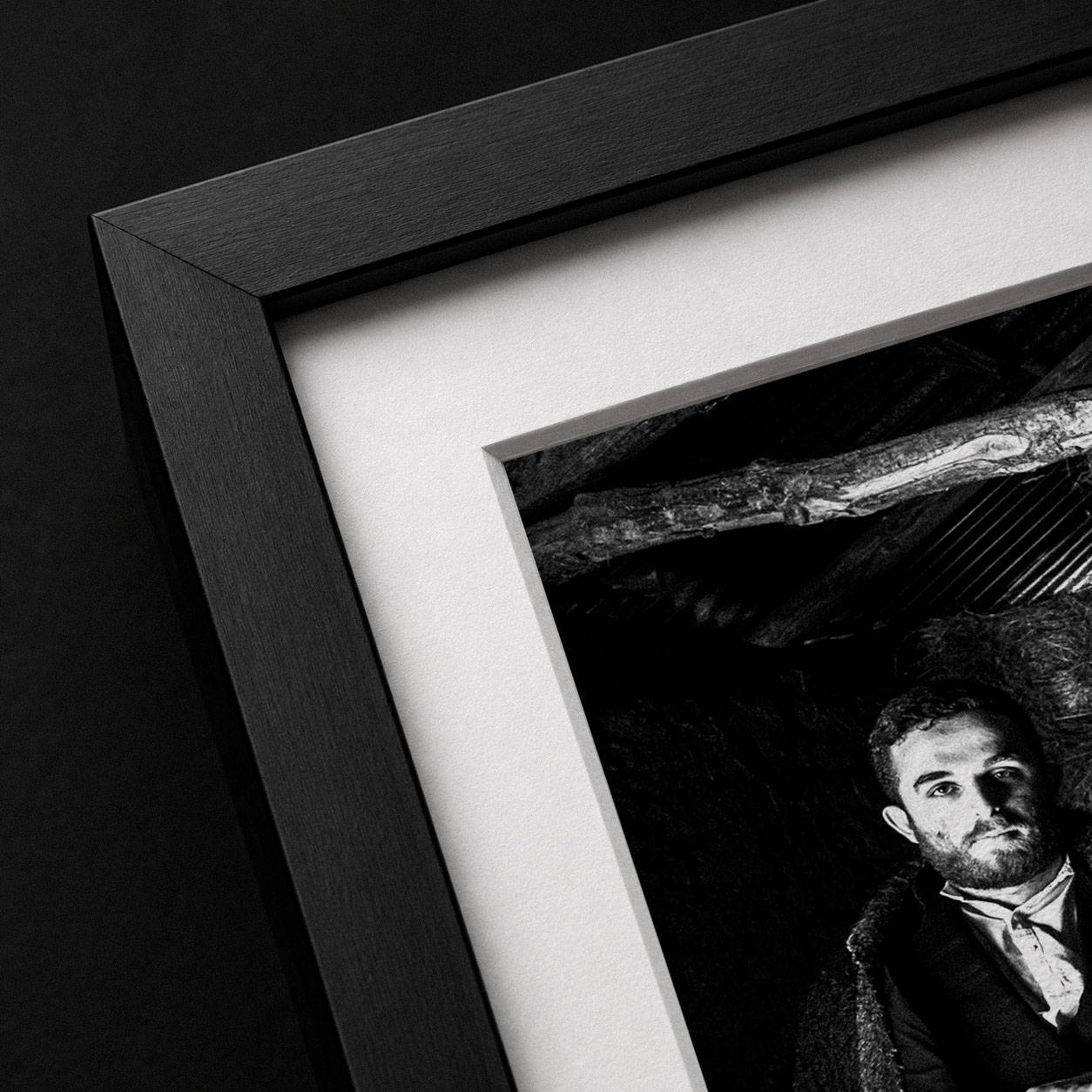 Close-up detail of a black solid oak frame with white mat surrounding a high-contrast black-and-white fine-art photograph.