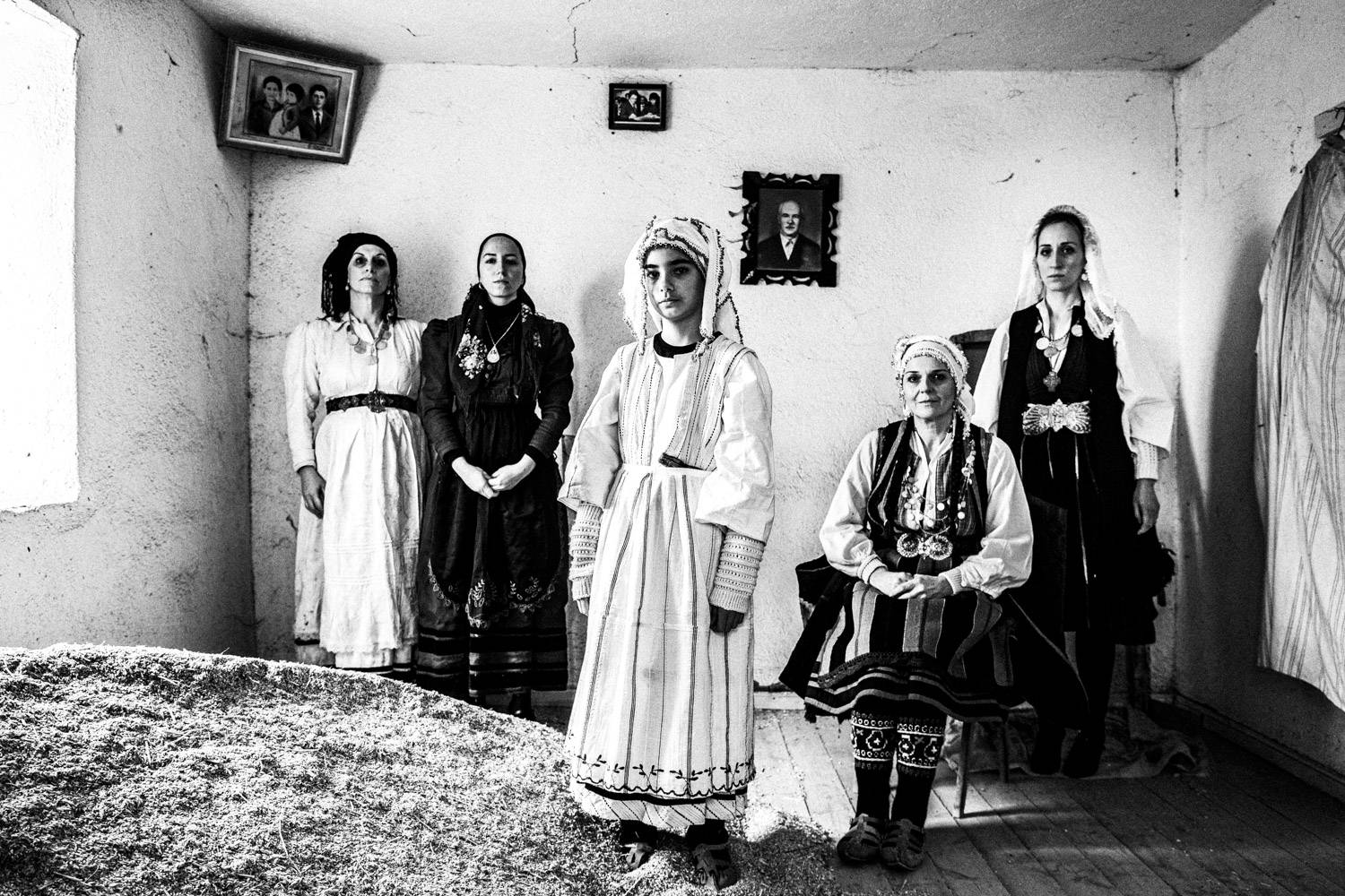 Portrait of four women and a girl wearing the local folklore dresses, inside an abandoned house. Ermakia, Ptolemaida, Macedonia, Greece. Black and white photograph by George Tatakis