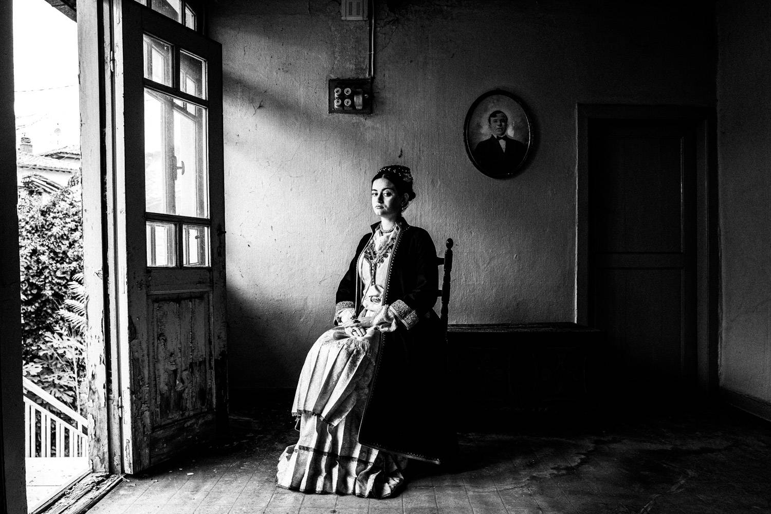 Sitting portrait of a woman inside a local abandoned house, wearing the traditional local attire. Veria, Imathia, Macedonia, Greece. Black and white photograph by George Tatakis