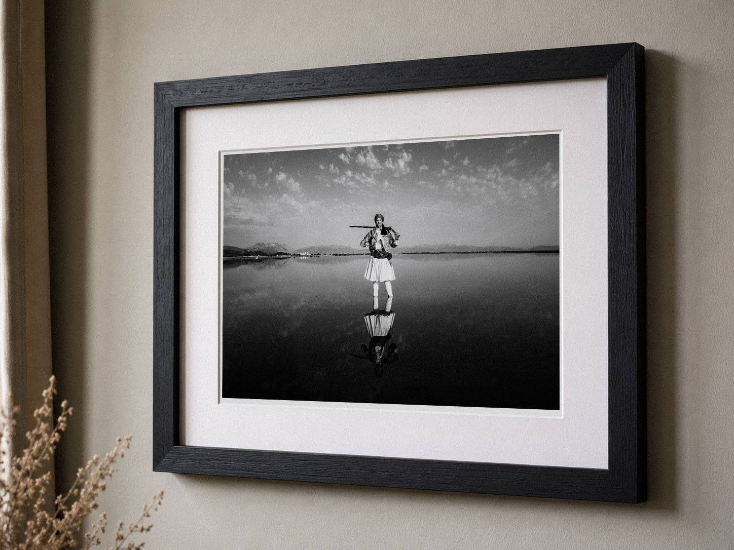 Framed black-and-white fine-art photograph displayed on a neutral wall in a minimalist interior, featuring a black solid oak frame and white mat.